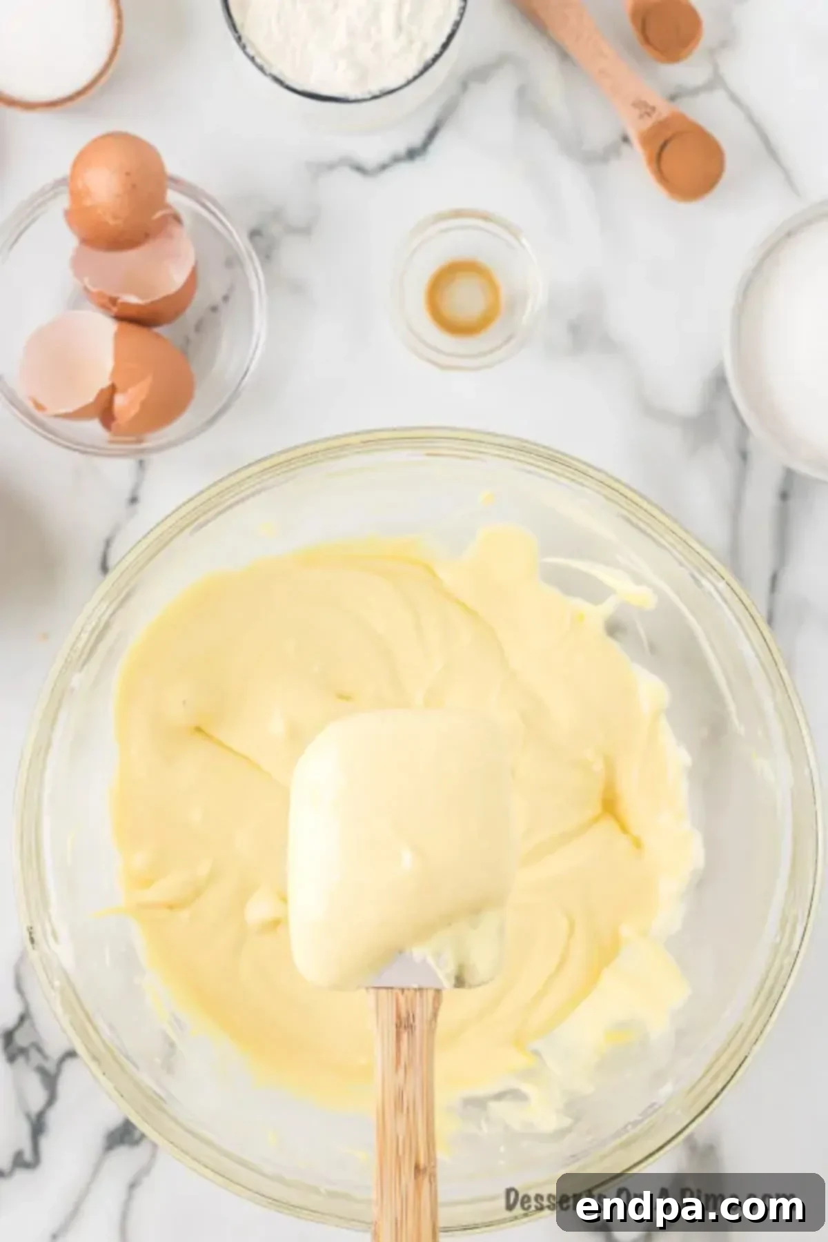 Eggs and vanilla extract being mixed into the smooth cream cheese and sugar mixture.