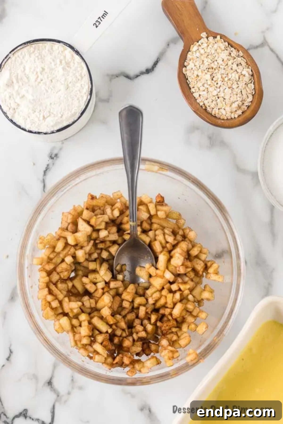 Finely chopped Granny Smith apples mixed with granulated sugar, ground cinnamon, and ground nutmeg in a small bowl.