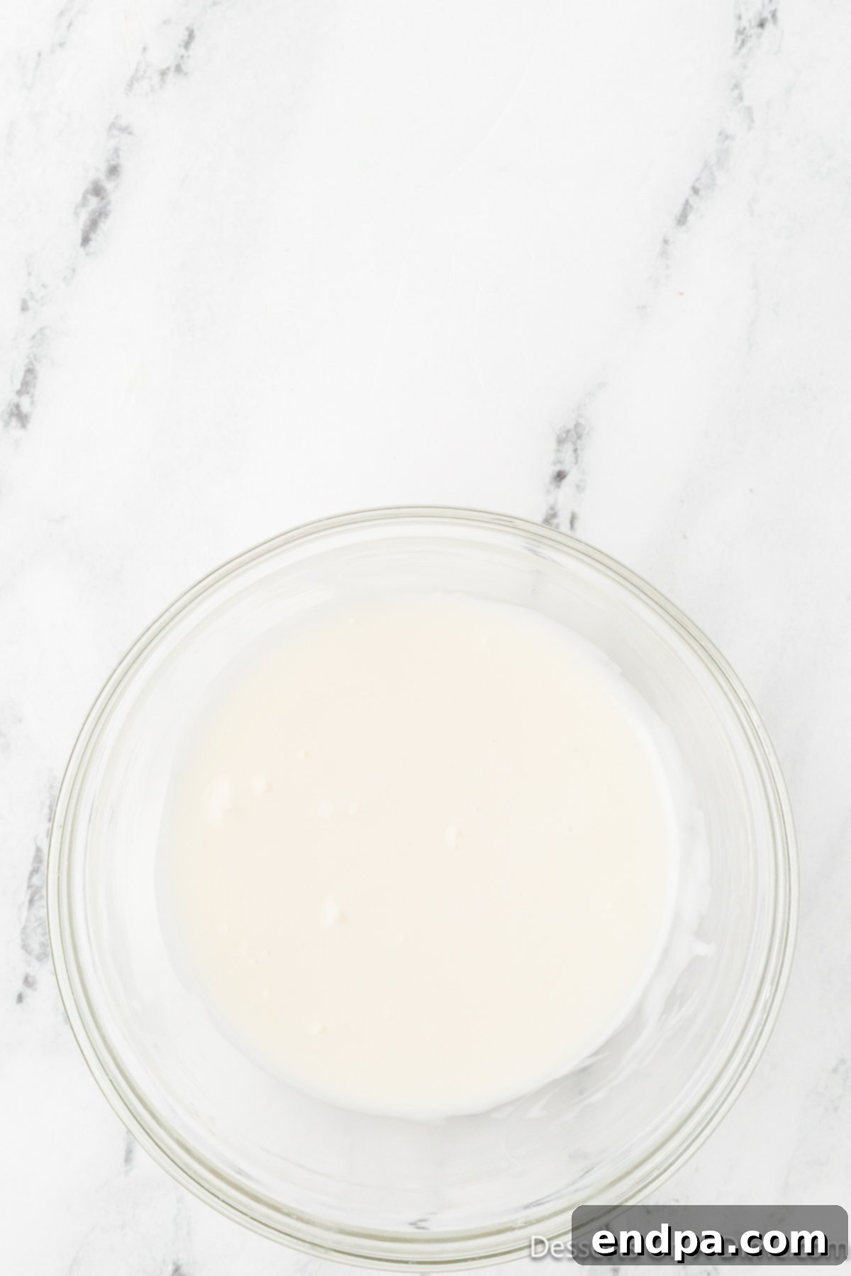 Powdered sugar and pineapple juice are vigorously whisked together in a bowl to create a smooth, pourable glaze.