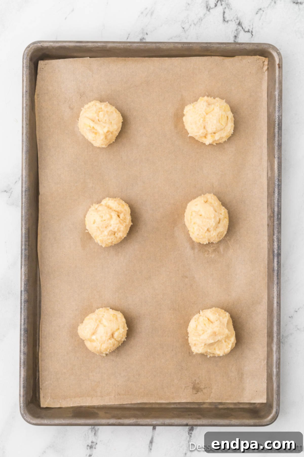 Uniform balls of cookie dough are scooped and carefully placed onto a parchment-lined baking sheet, spaced for baking.