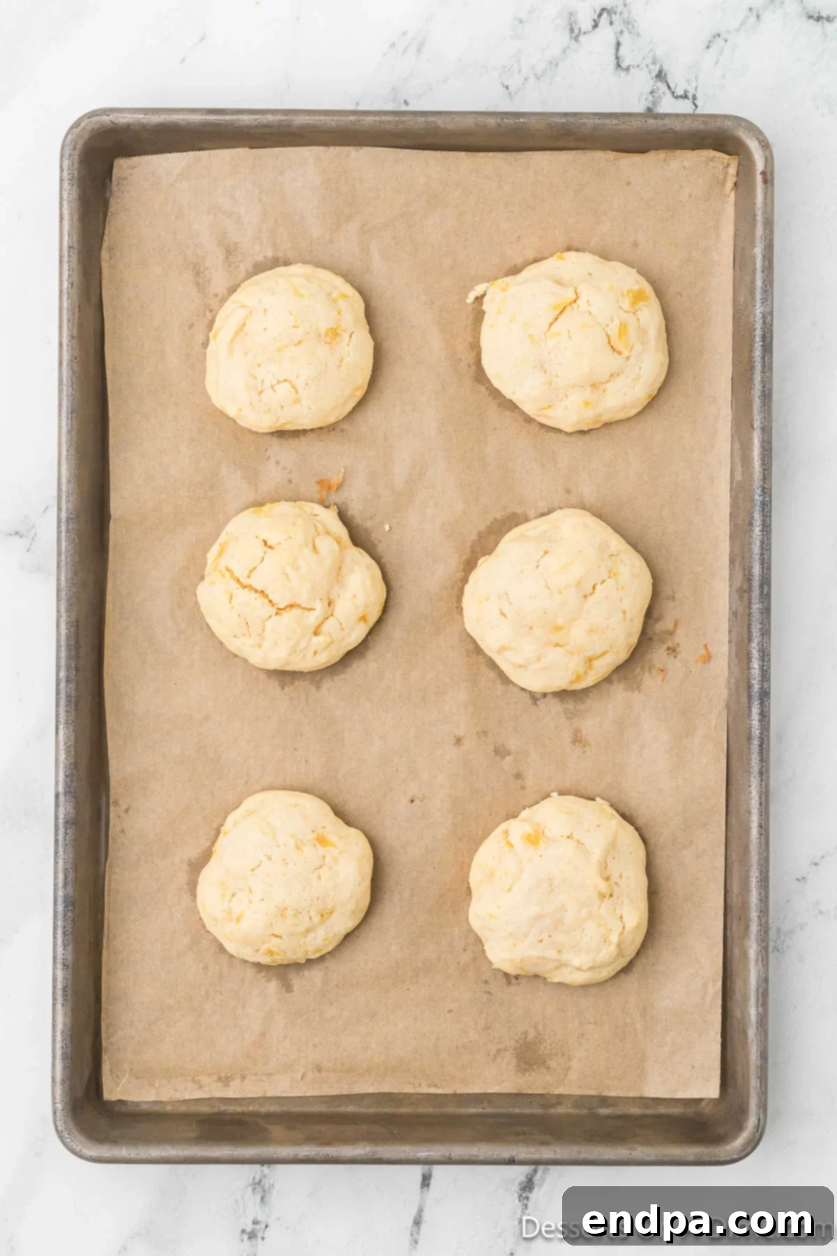 Freshly baked pineapple cookies cooling on the baking sheet after being removed from the oven, centers soft and edges golden.