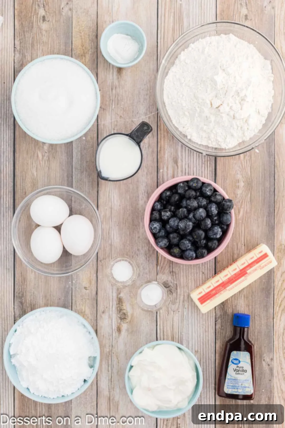 Sapphire Swirl Cake 3 A flat lay of ingredients for blueberry bundt cake, including flour, baking soda, butter, eggs, sour cream, and fresh blueberries.