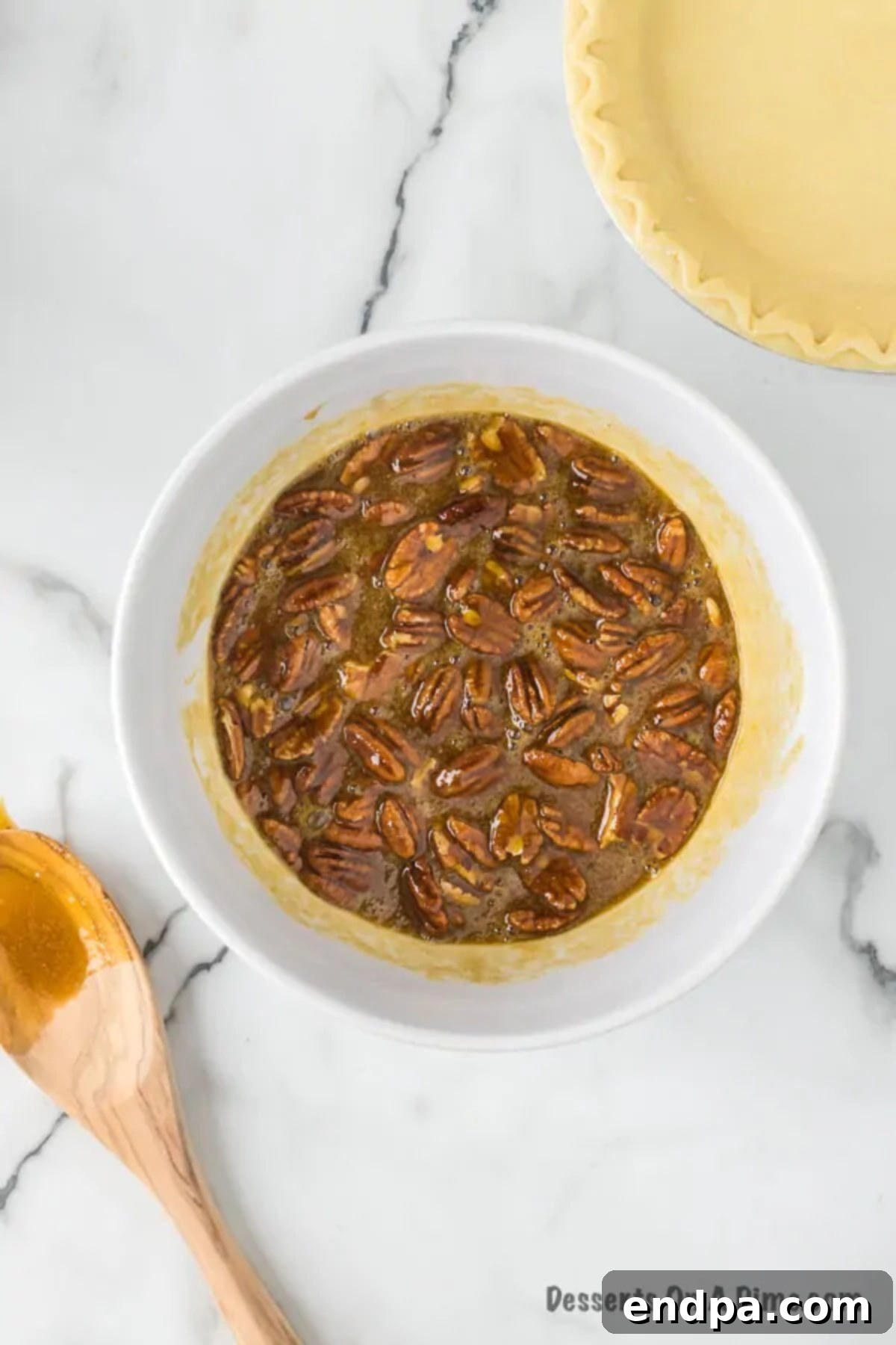 Pecan halves being gently folded into the prepared pie filling mixture in a glass bowl.