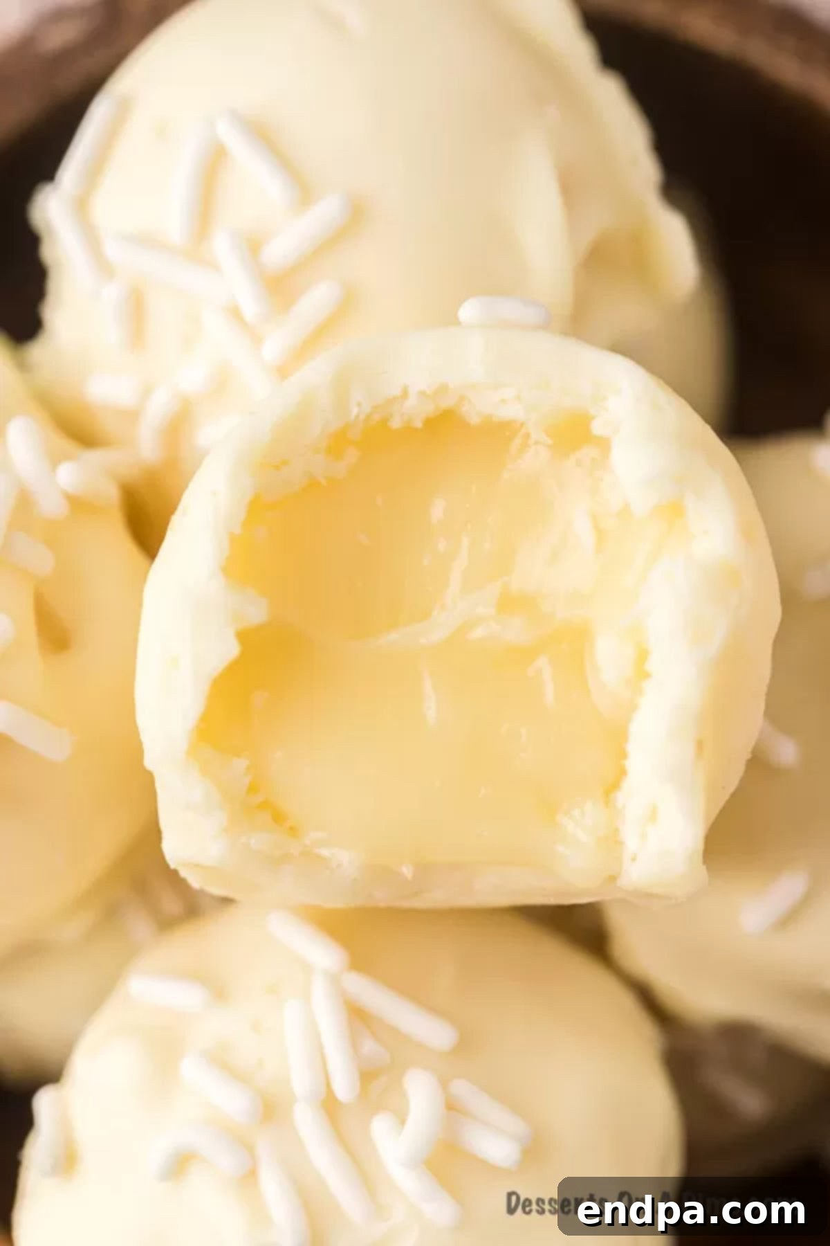 A stack of perfectly crafted White Chocolate Truffles, garnished with delicate white sprinkles, resting on a serving platter.