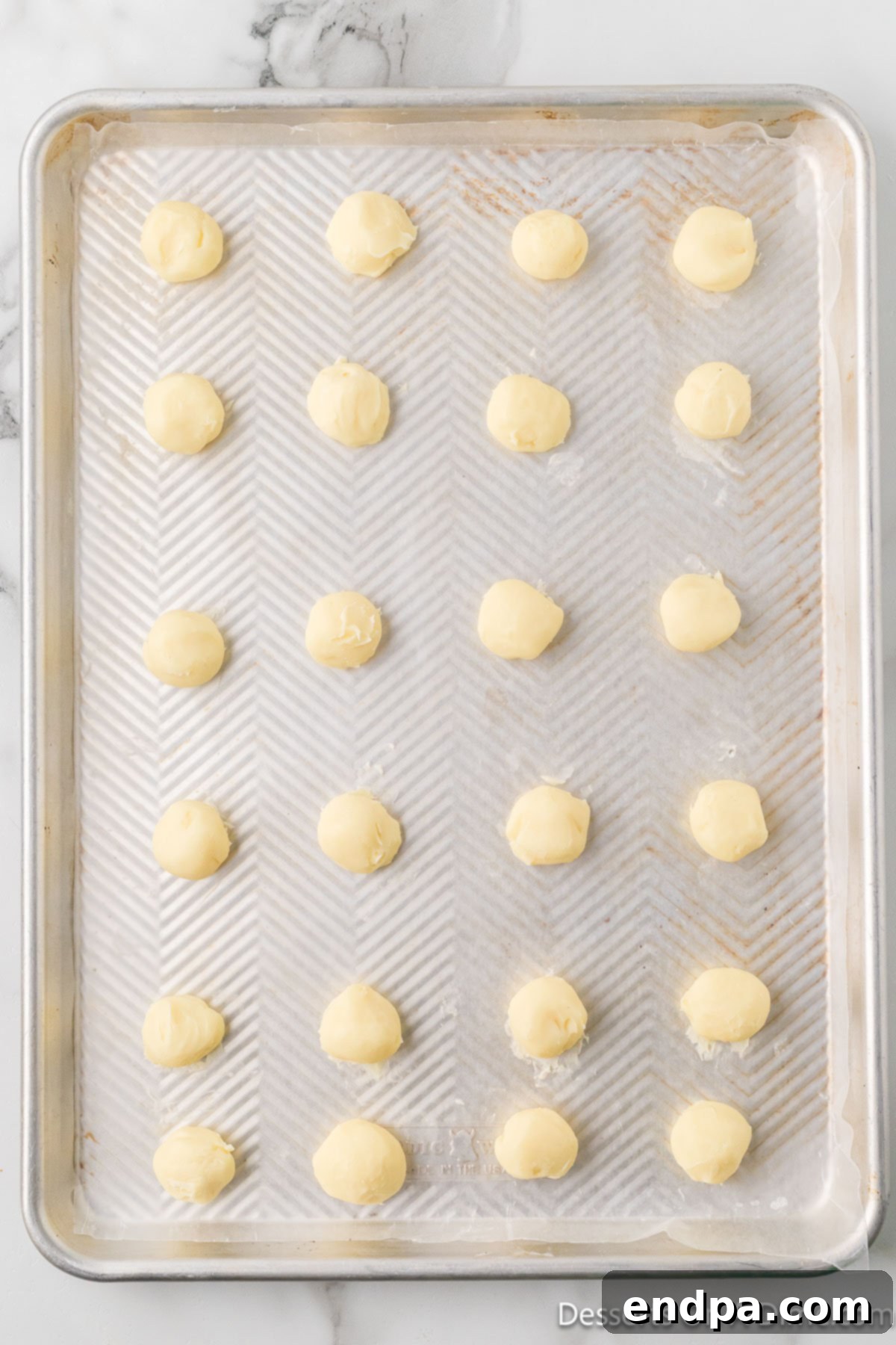 Rolled white chocolate truffles resting on parchment paper on a baking sheet, ready for freezing.