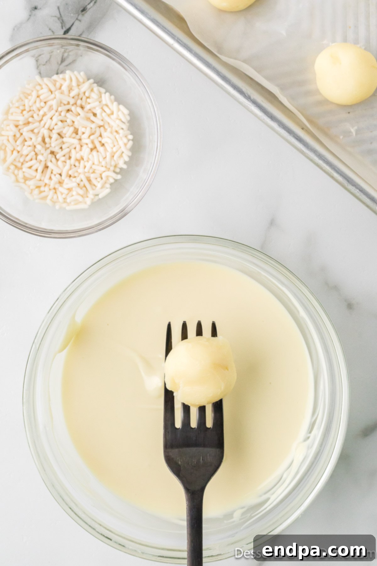 A truffle being dipped into melted white chocolate, ensuring a full and even coating.