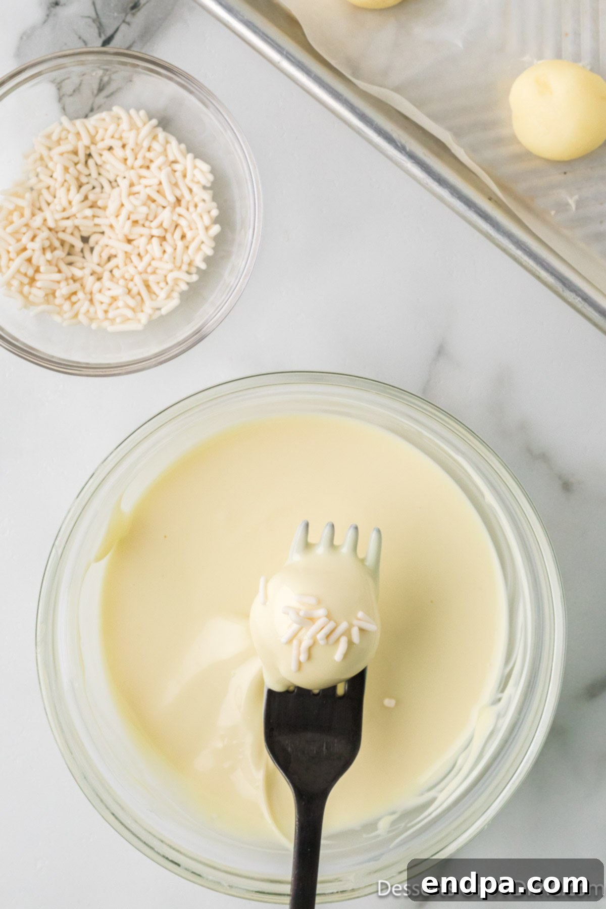 A freshly dipped white chocolate truffle, glistening with melted chocolate, placed on parchment paper.