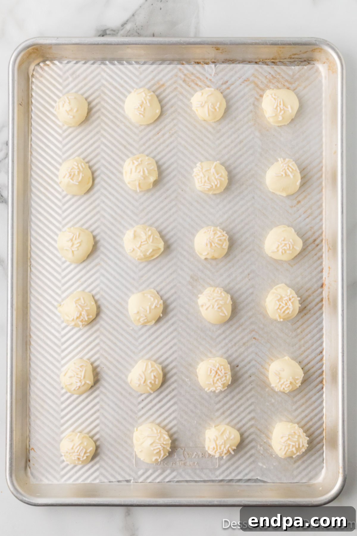 White chocolate truffles on parchment paper, freshly dipped and decorated with white sprinkles, ready to harden.