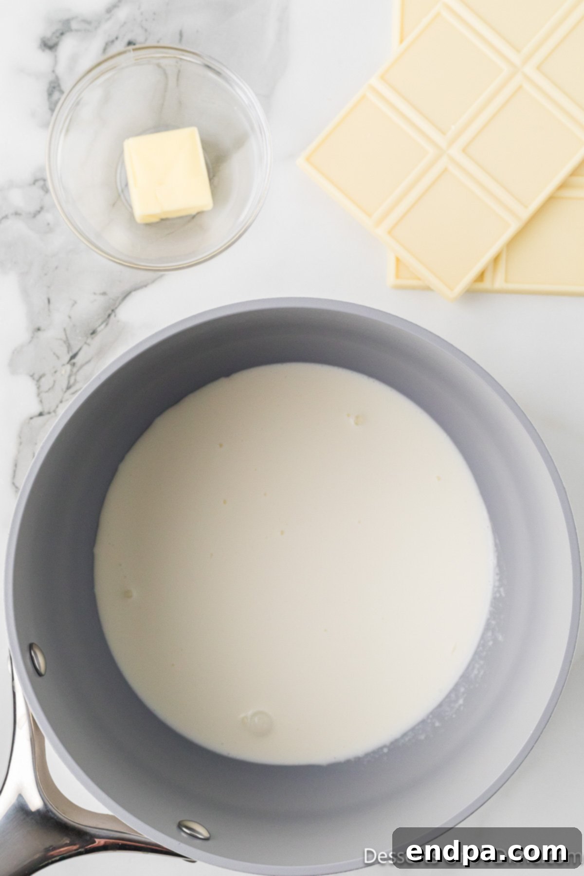 Heavy whipping cream simmering gently in a small saucepan on the stovetop.