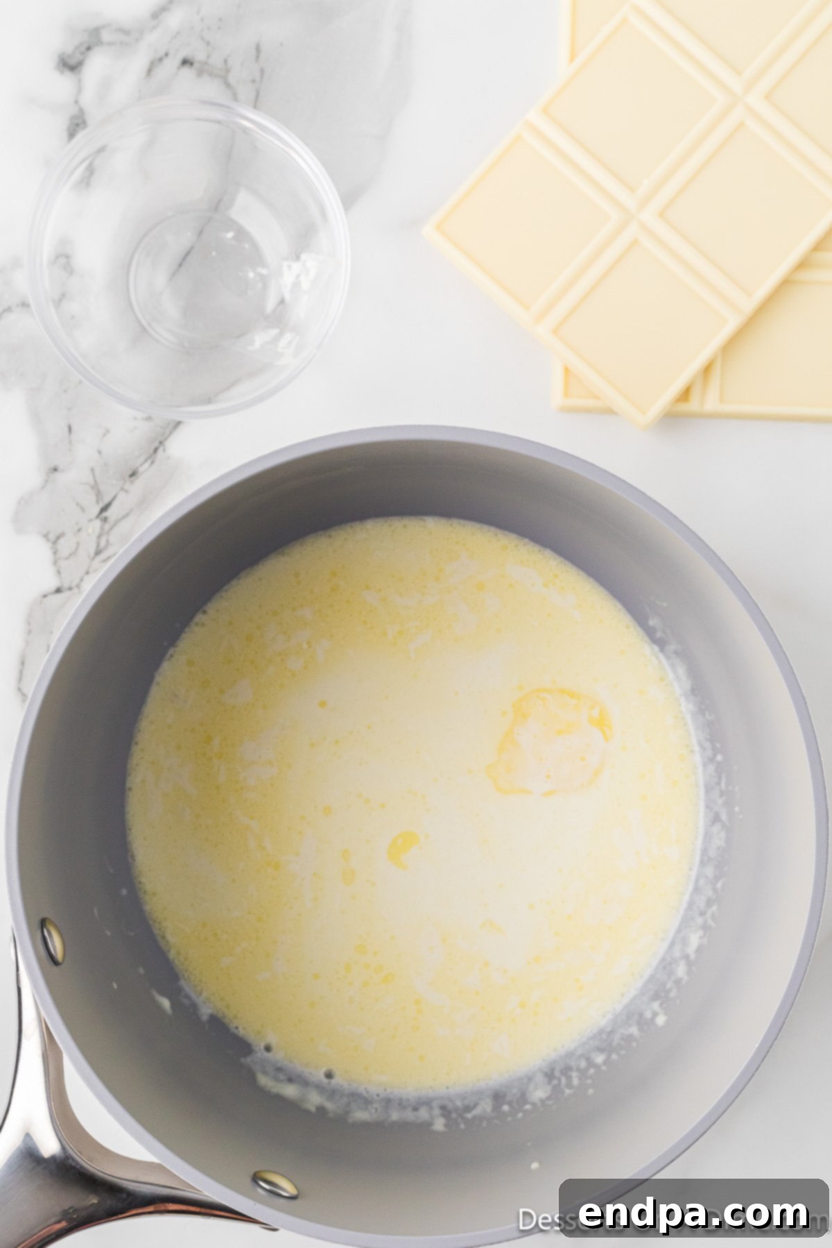 Chunks of white chocolate baking bars are added to the warm cream and butter mixture in the saucepan.