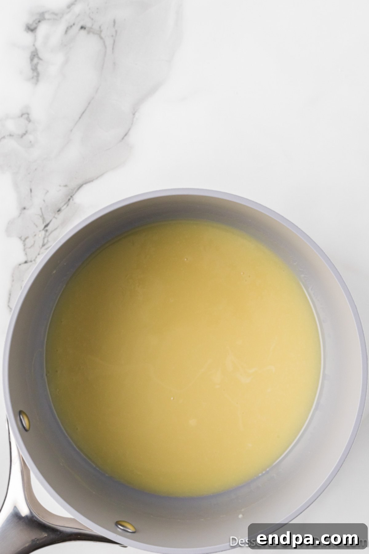 The smooth white chocolate ganache being poured into a glass bowl, ready for chilling.