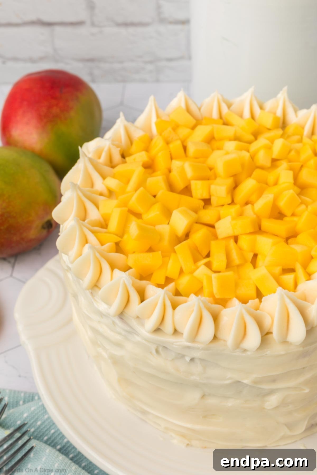 Diced fresh mangoes artfully arranged on top of the frosted mango cake, within the piped frosting border.