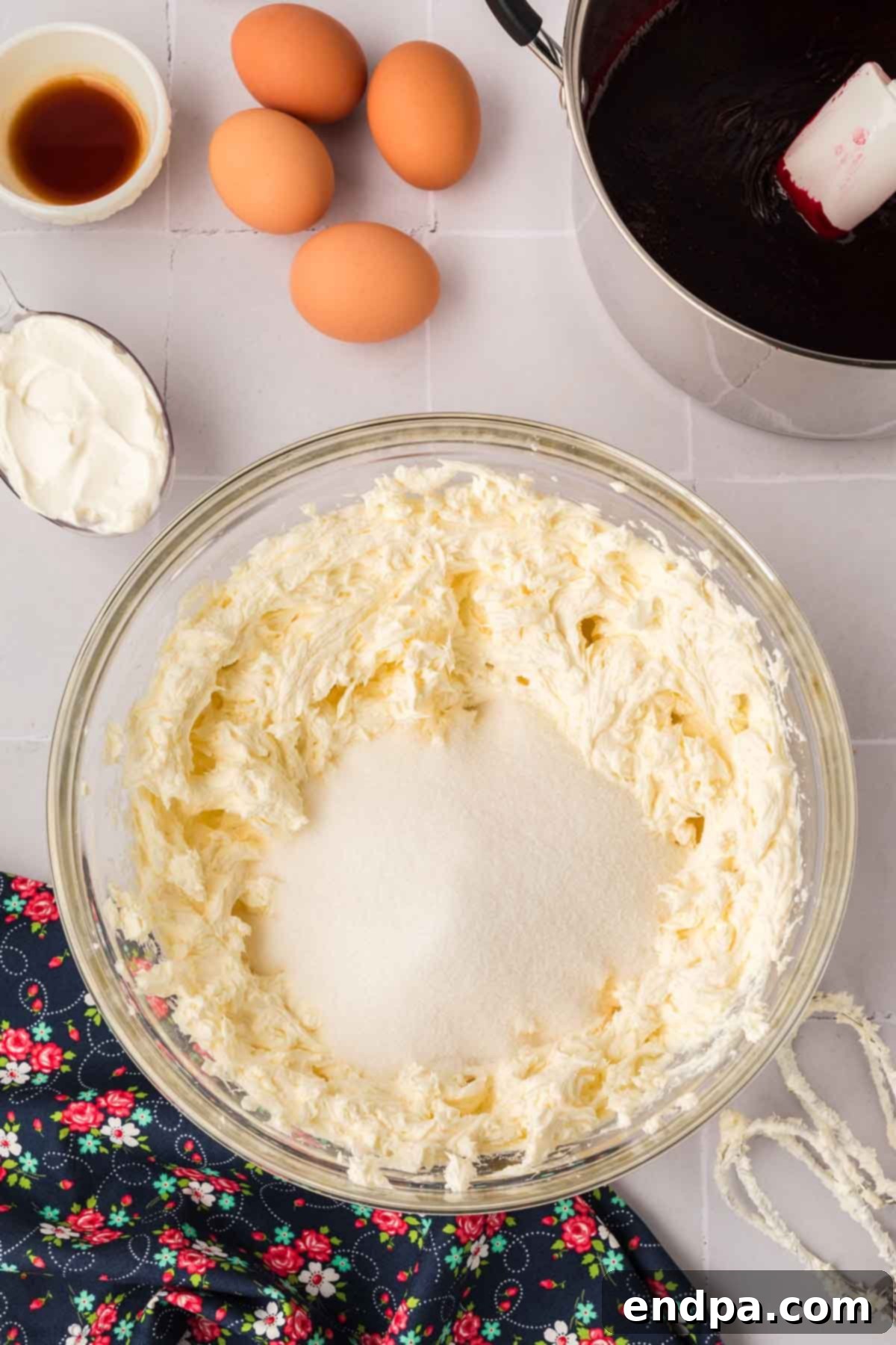Granulated sugar being added to the fluffy cream cheese mixture in a stand mixer, ready to be combined.