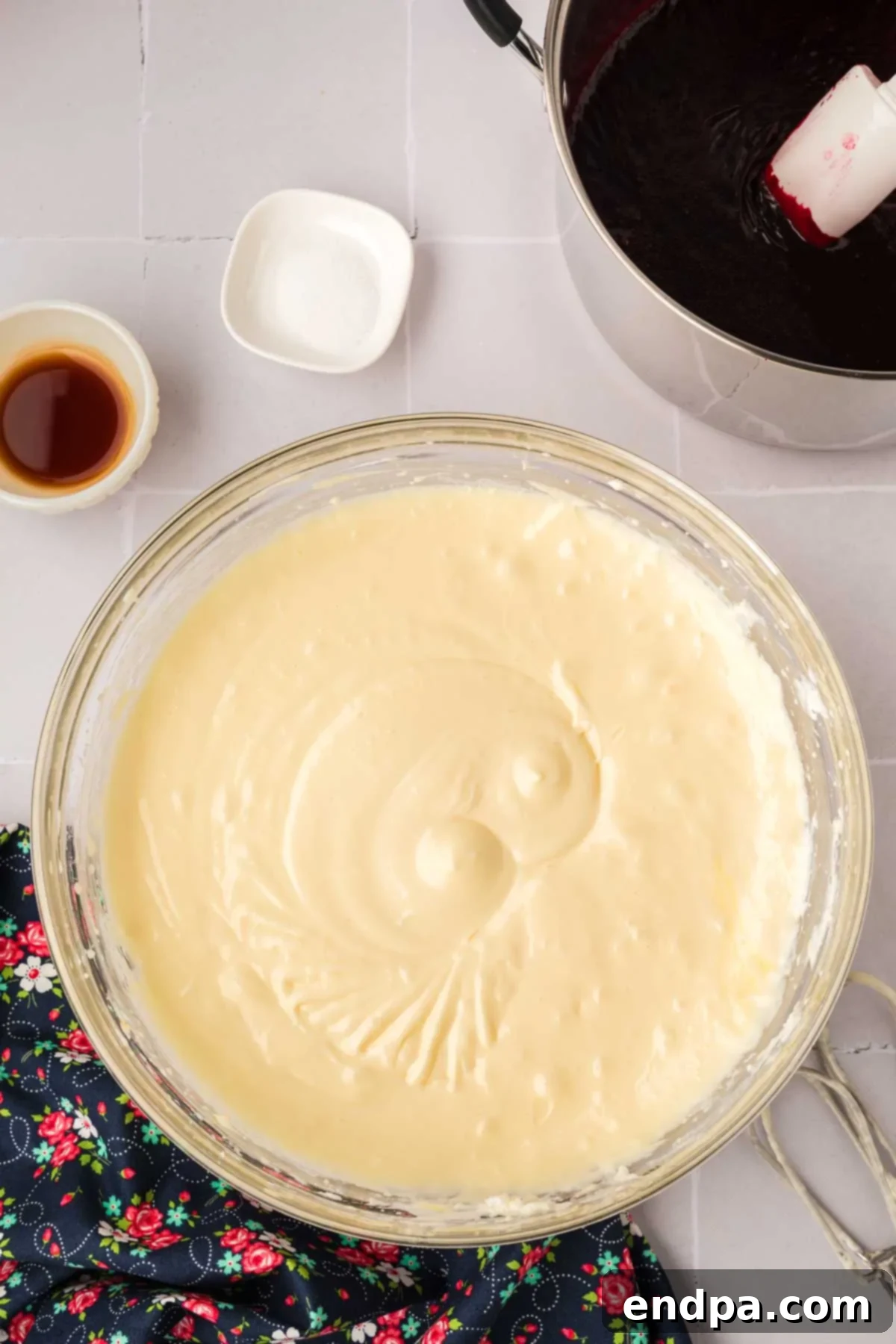 Sour cream being mixed into the cream cheese and sugar mixture in a stand mixer, creating a smooth cheesecake filling.