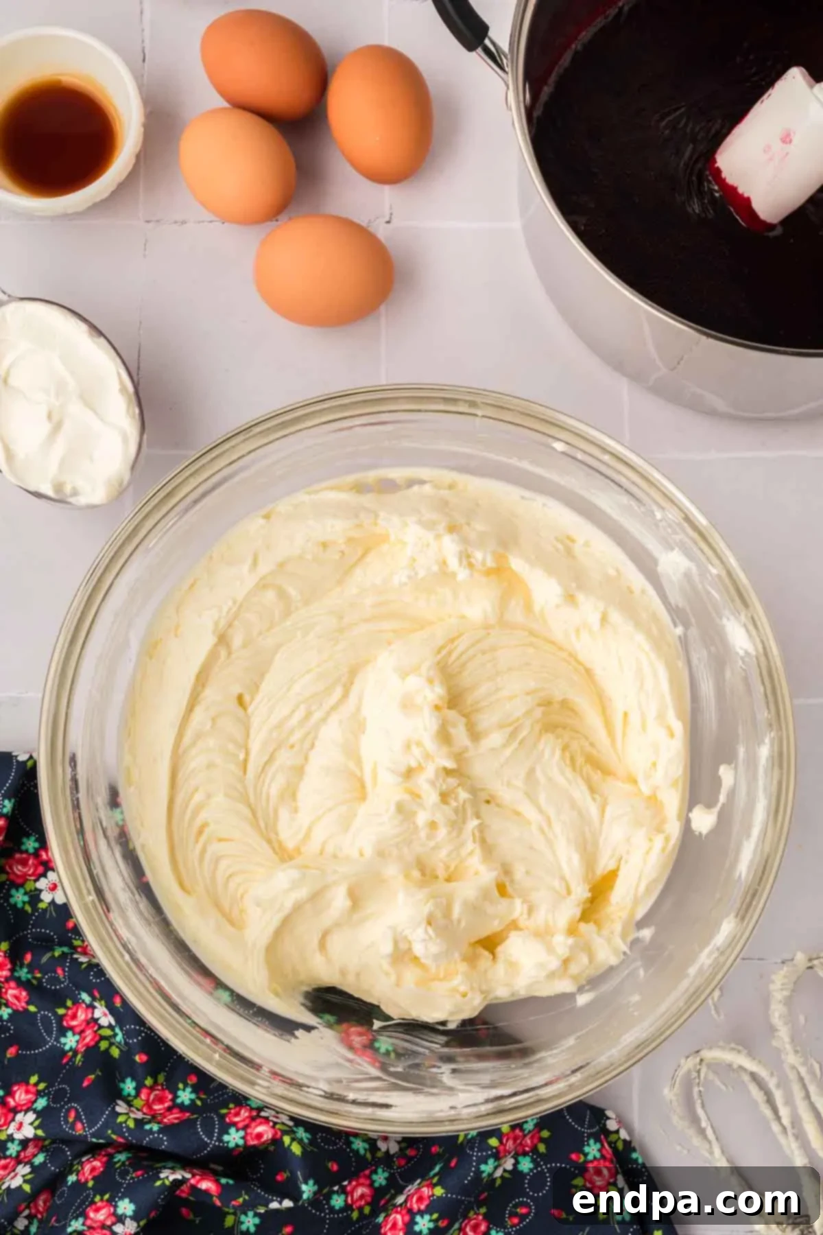 Large eggs being added one at a time to the cheesecake filling in a mixing bowl, ensuring each is incorporated before adding the next.