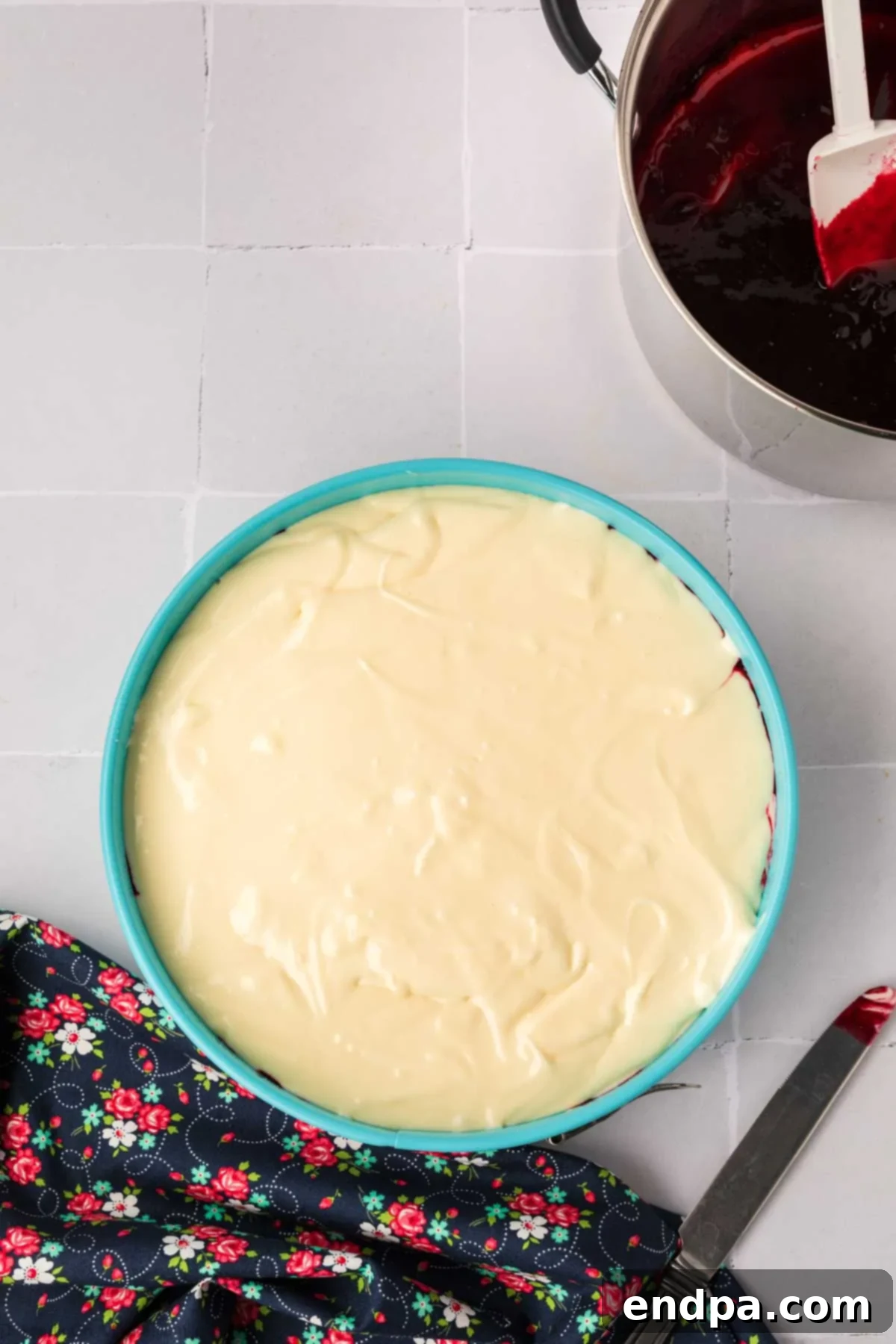 The first layer of creamy cheesecake filling poured into the baked crust, with blackberry puree spooned on top, ready for swirling.