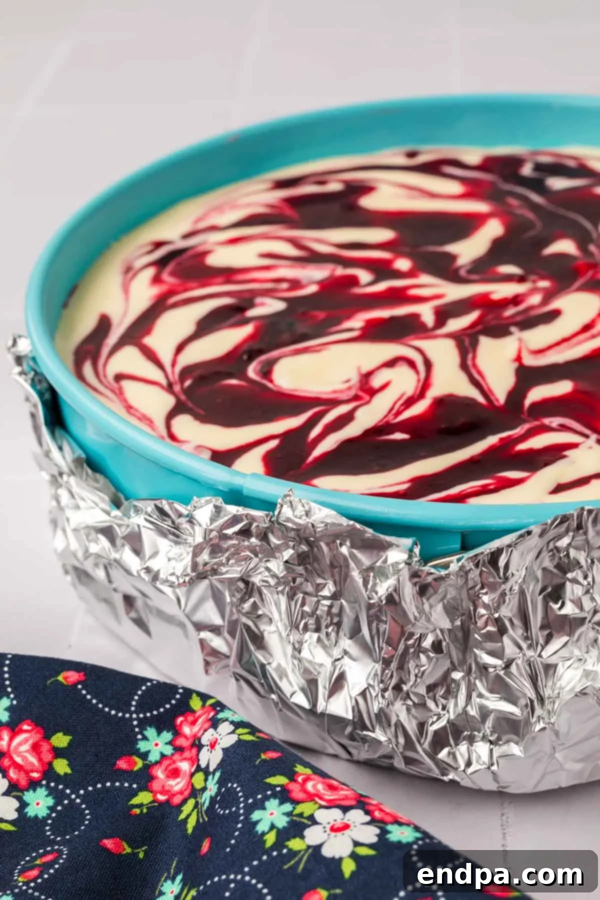 A springform pan containing the blackberry cheesecake, wrapped in aluminum foil around the base to prevent water seepage during a water bath.