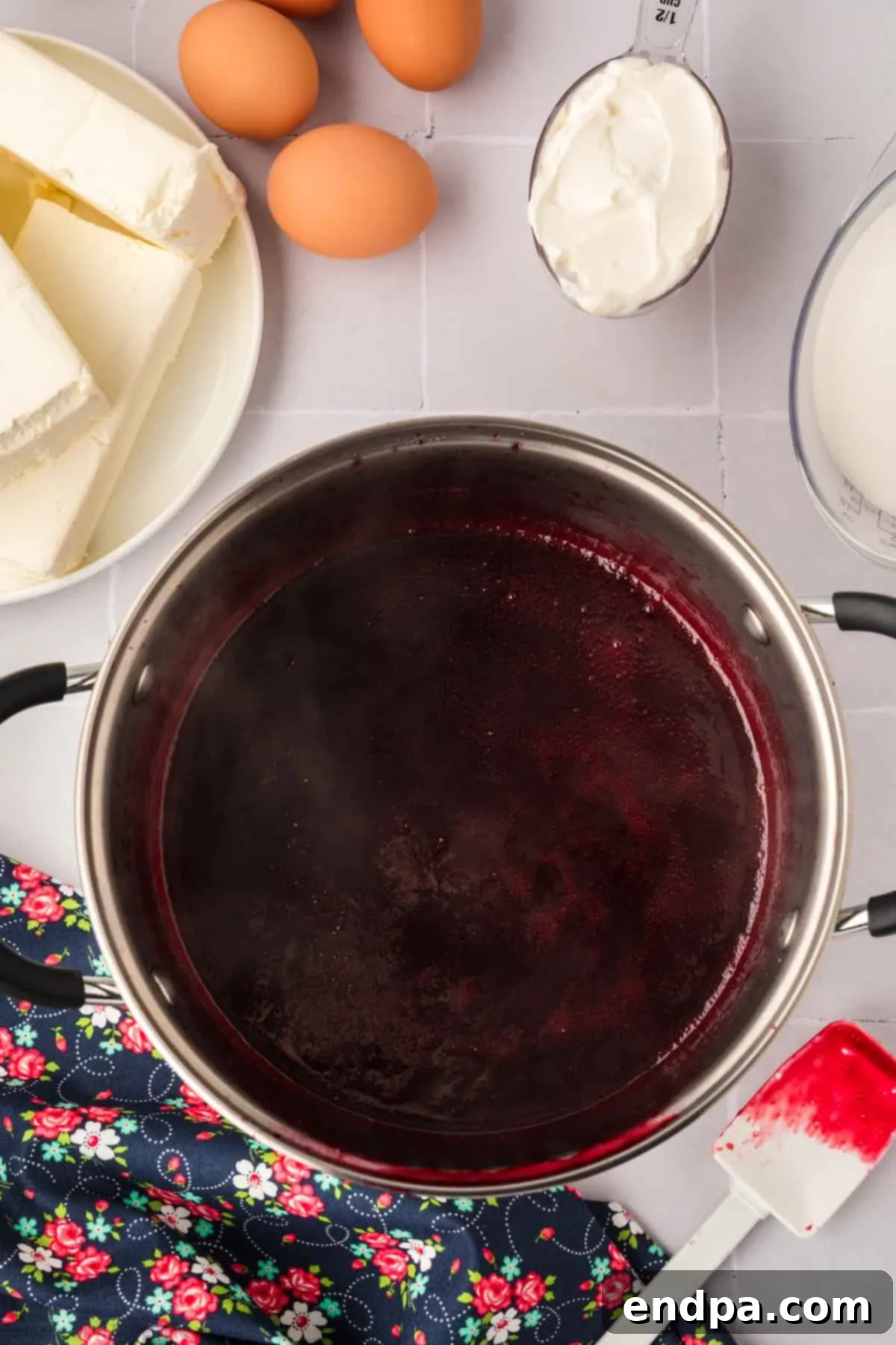 Strained blackberry puree in a saucepan, with a cornstarch slurry being added and stirred in to thicken the sauce.