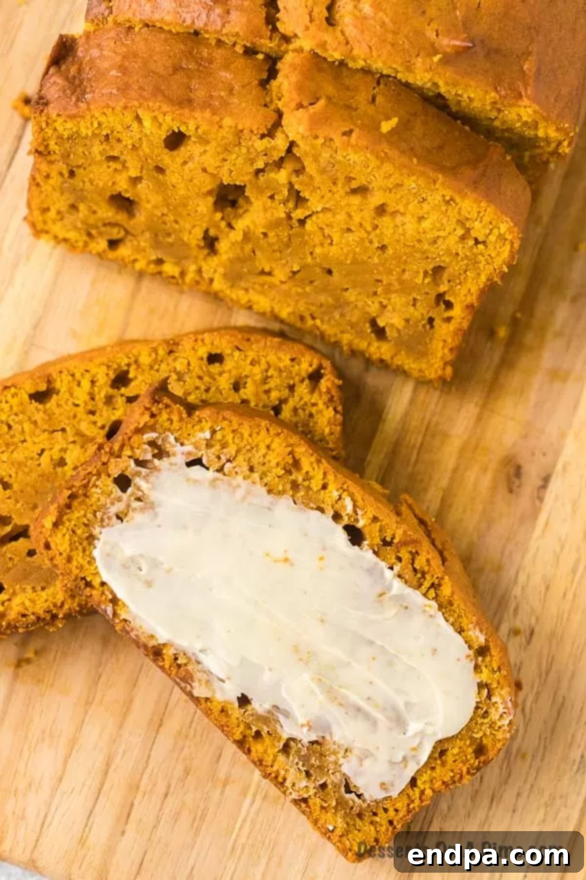 Pumpkin bread sliced on a wooden plate, with one piece buttered, showcasing its moist texture.
