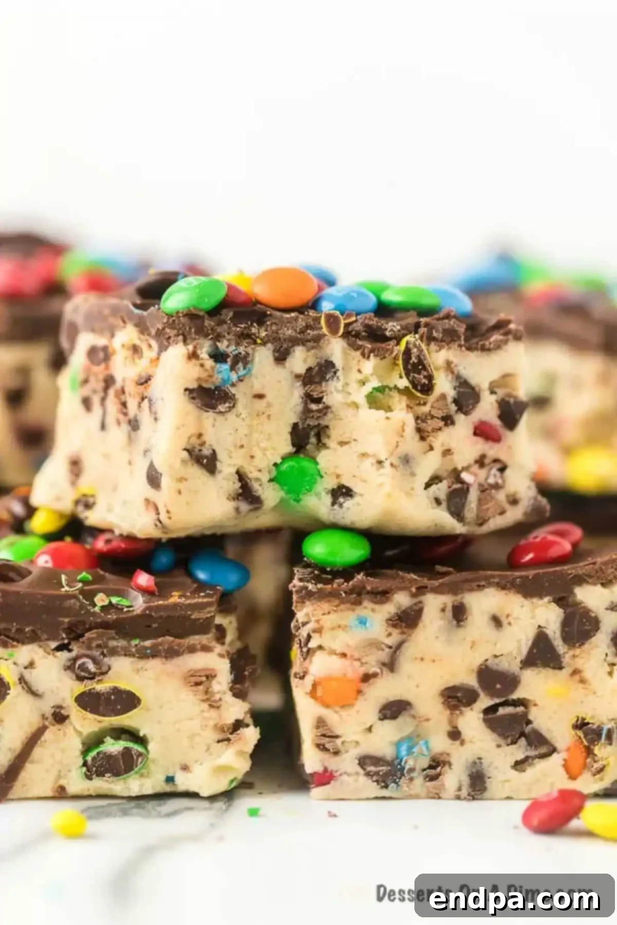 Several neatly cut cookie dough bars stacked, showcasing their layers of dough, chocolate chips, and M&M's.