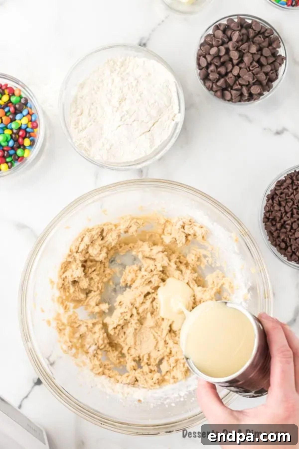 Sweetened condensed milk being poured into the mixing bowl with other cookie dough ingredients.