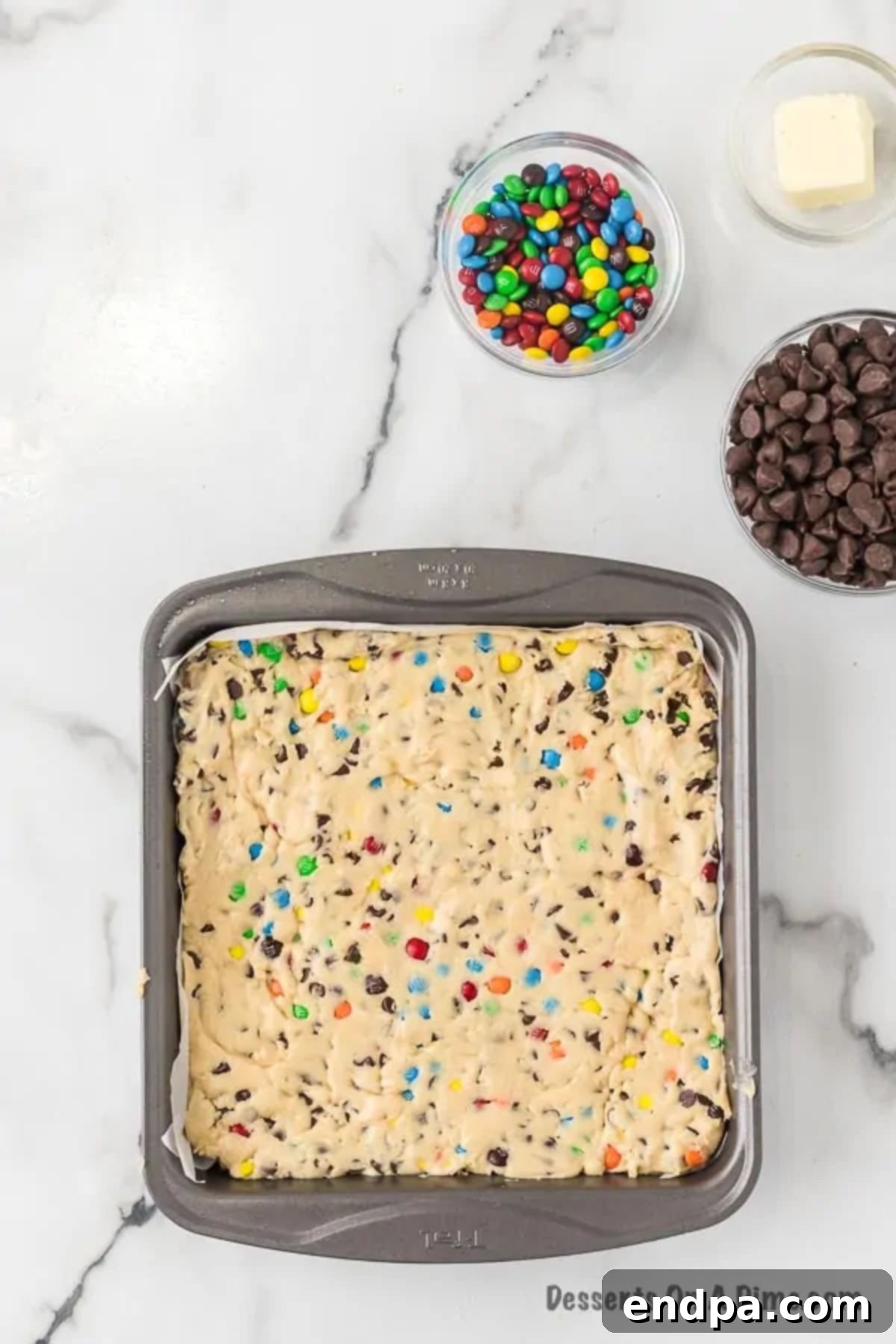 The finished cookie dough pressed evenly into a square baking pan lined with parchment paper.