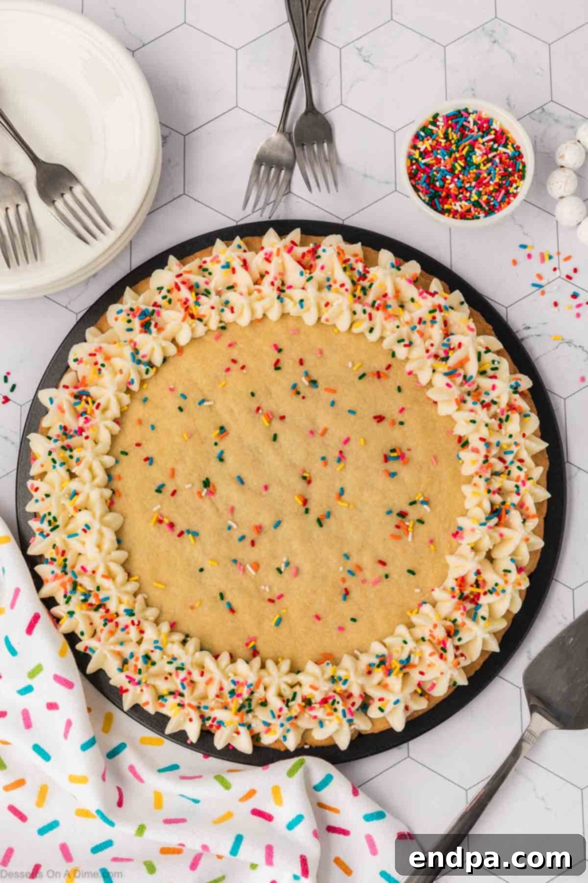 A beautifully decorated Sugar Cookie Cake with vanilla buttercream frosting piped elegantly around the edges and colorful sprinkles scattered on top.