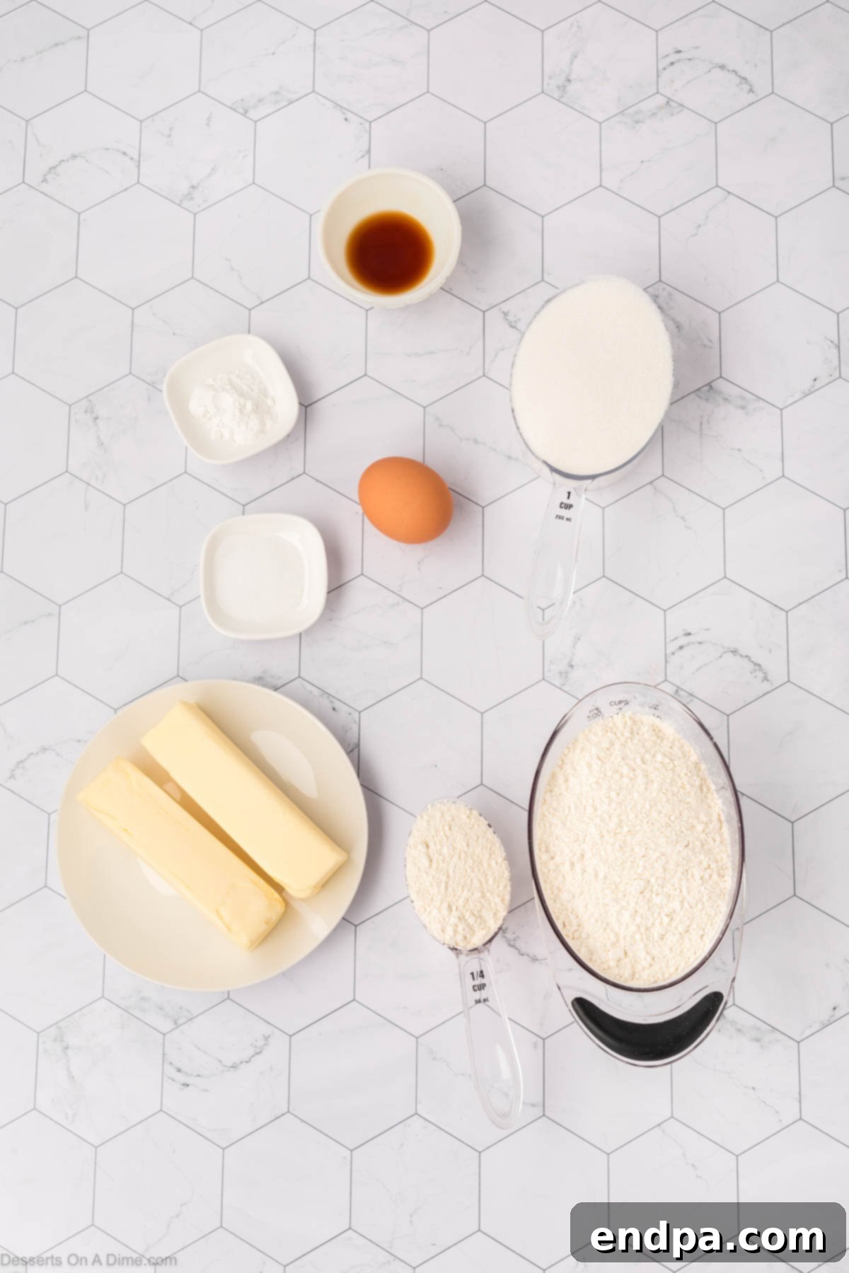 A collection of key ingredients for sugar cookie cake, including unsalted butter, an egg, vanilla extract, and all-purpose flour, neatly arranged on a counter.