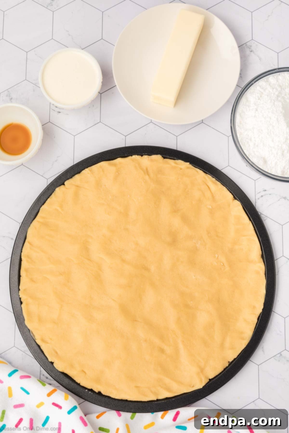 The sugar cookie dough evenly pressed into the round cookie cake pan, ready for baking.