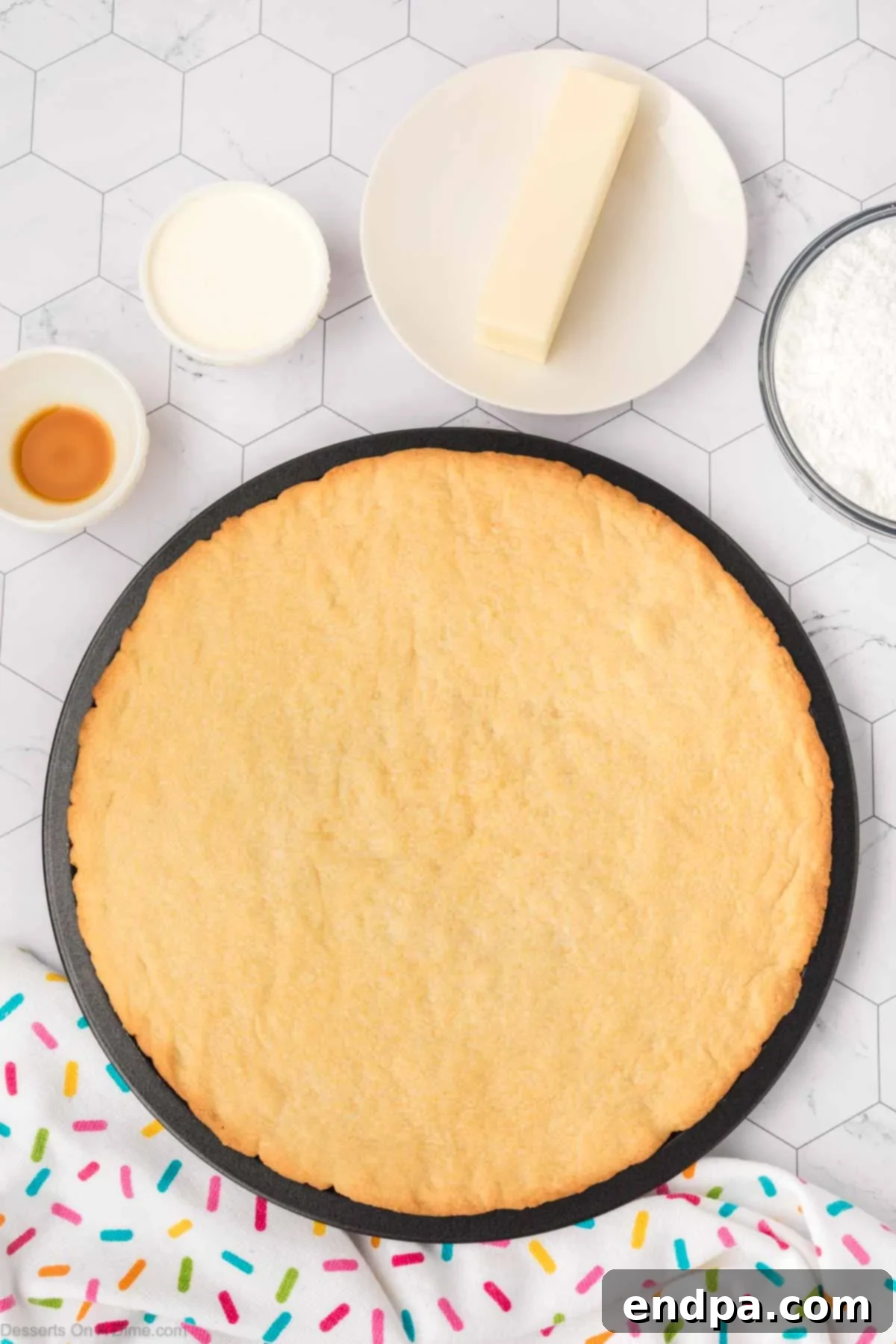 The baked sugar cookie cake, showing golden-brown edges, cooling in the pan after being removed from the oven.