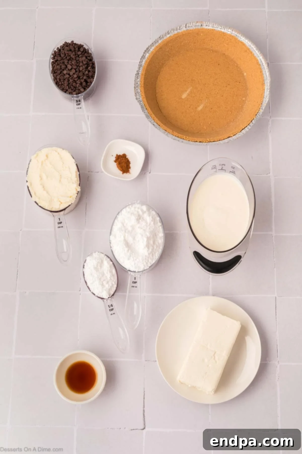 A vibrant flat lay of ingredients for cannoli pie, featuring cream cheese, vanilla extract, heavy cream, powdered sugar, whole milk ricotta, cinnamon, mini chocolate chips, and a pre-made graham cracker crust, all laid out on a clean surface.