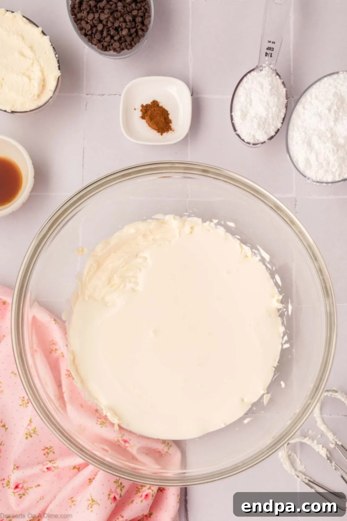 Heavy cream being added to the beaten cream cheese mixture in a mixing bowl.