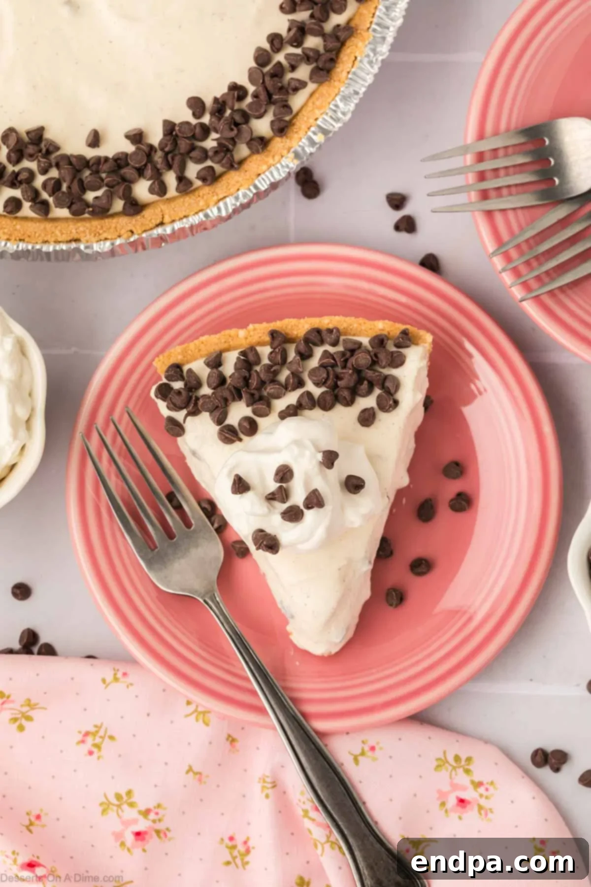 A delectable slice of cannoli pie, adorned with whipped cream and mini chocolate chips, presented on a white plate with a fork.