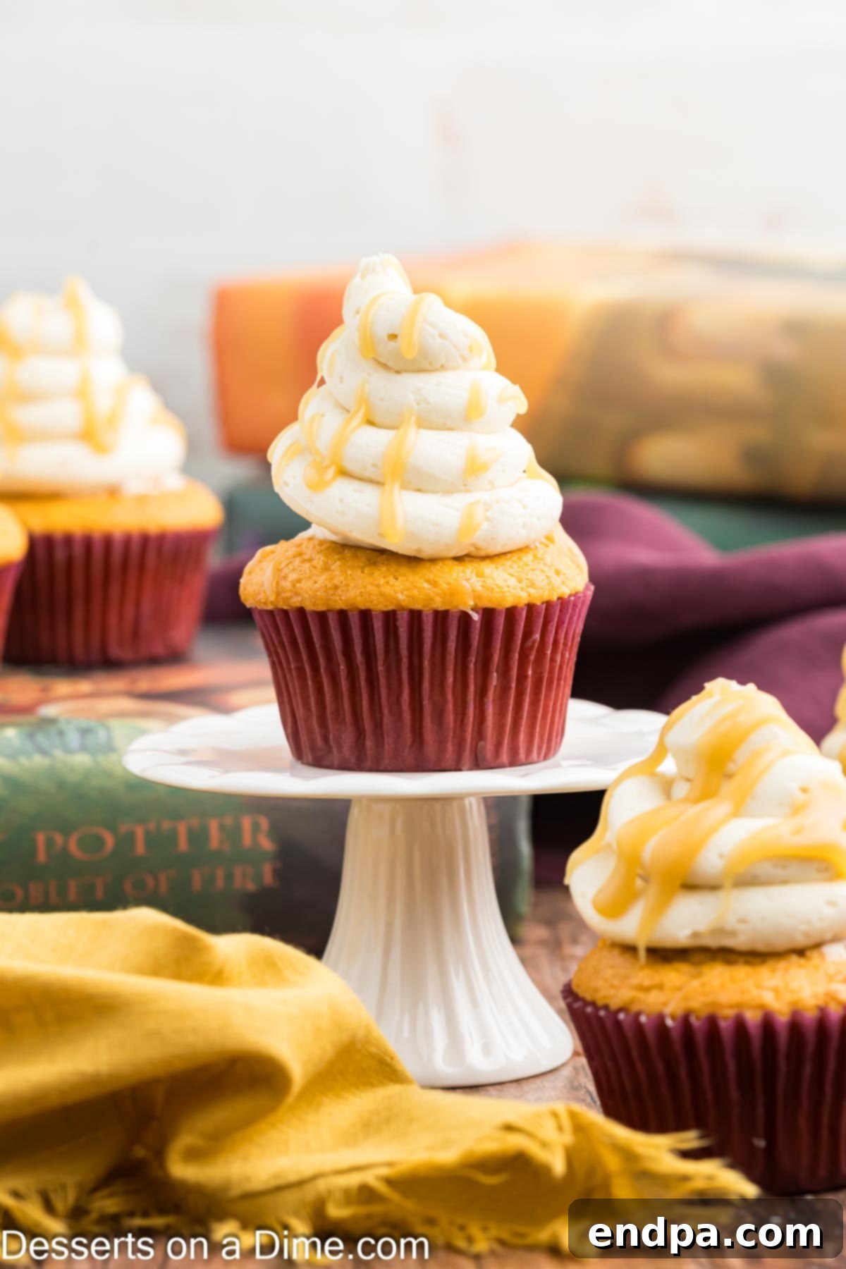 A single Harry Potter Butterbeer Cupcake on a decorative stand, highlighting its tall swirl of butterscotch frosting and delectable appeal.