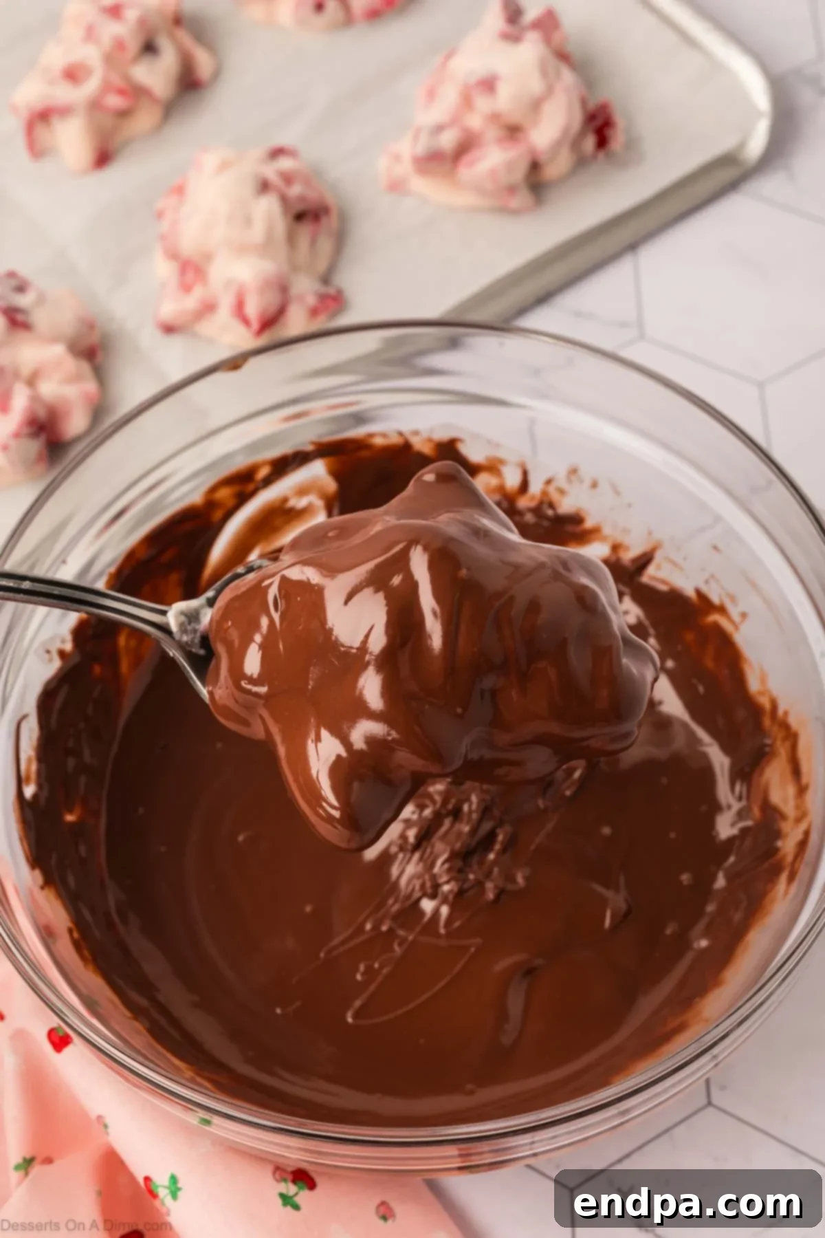 Frozen yogurt clusters being dipped into the melted chocolate using a spoon.