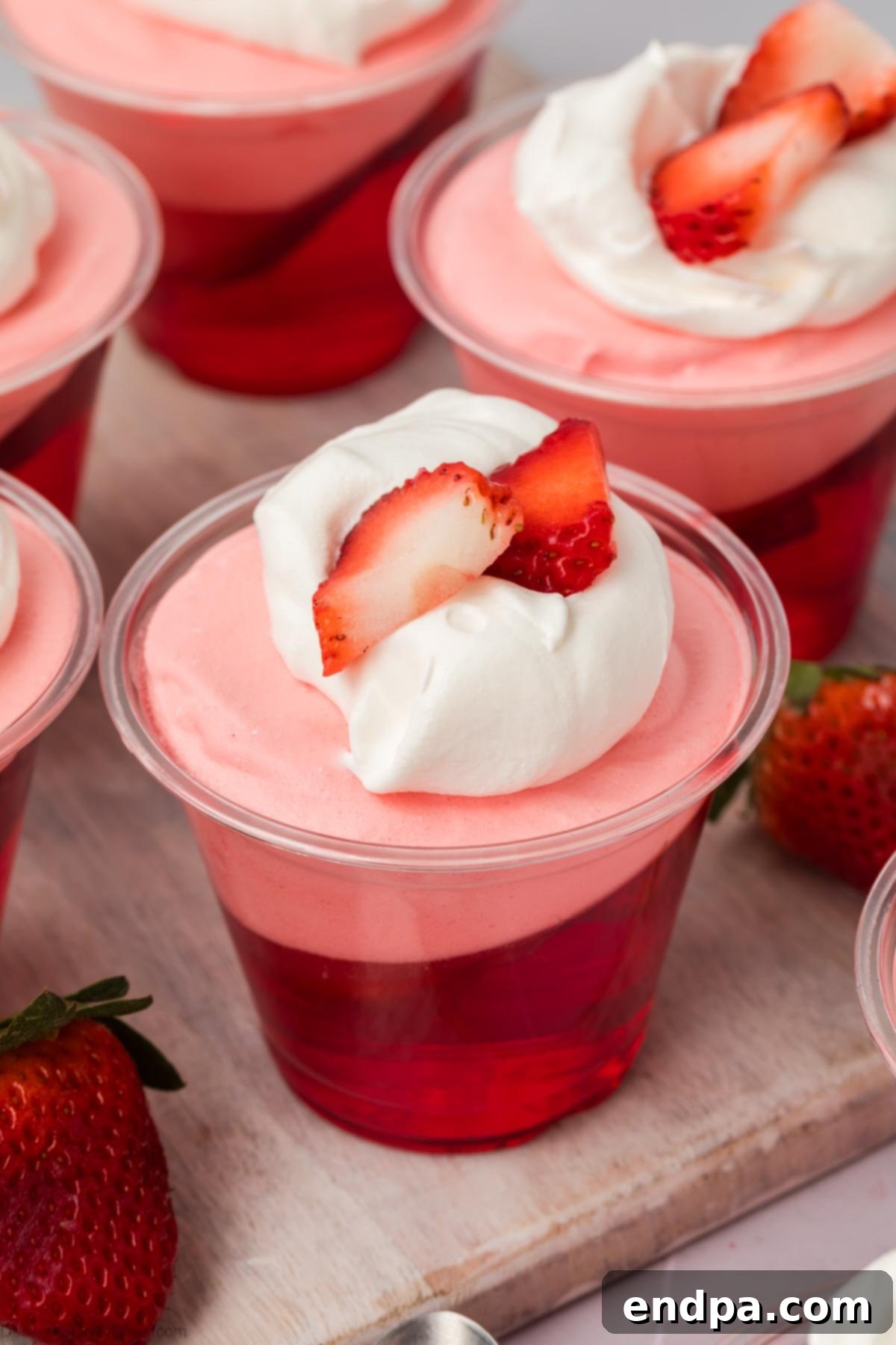 Several cups of beautifully layered strawberry jello parfaits garnished with fresh berries.