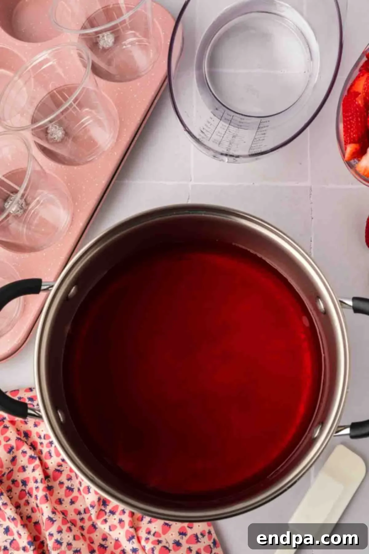 Strawberry Jello powder being stirred into hot water in a saucepan.