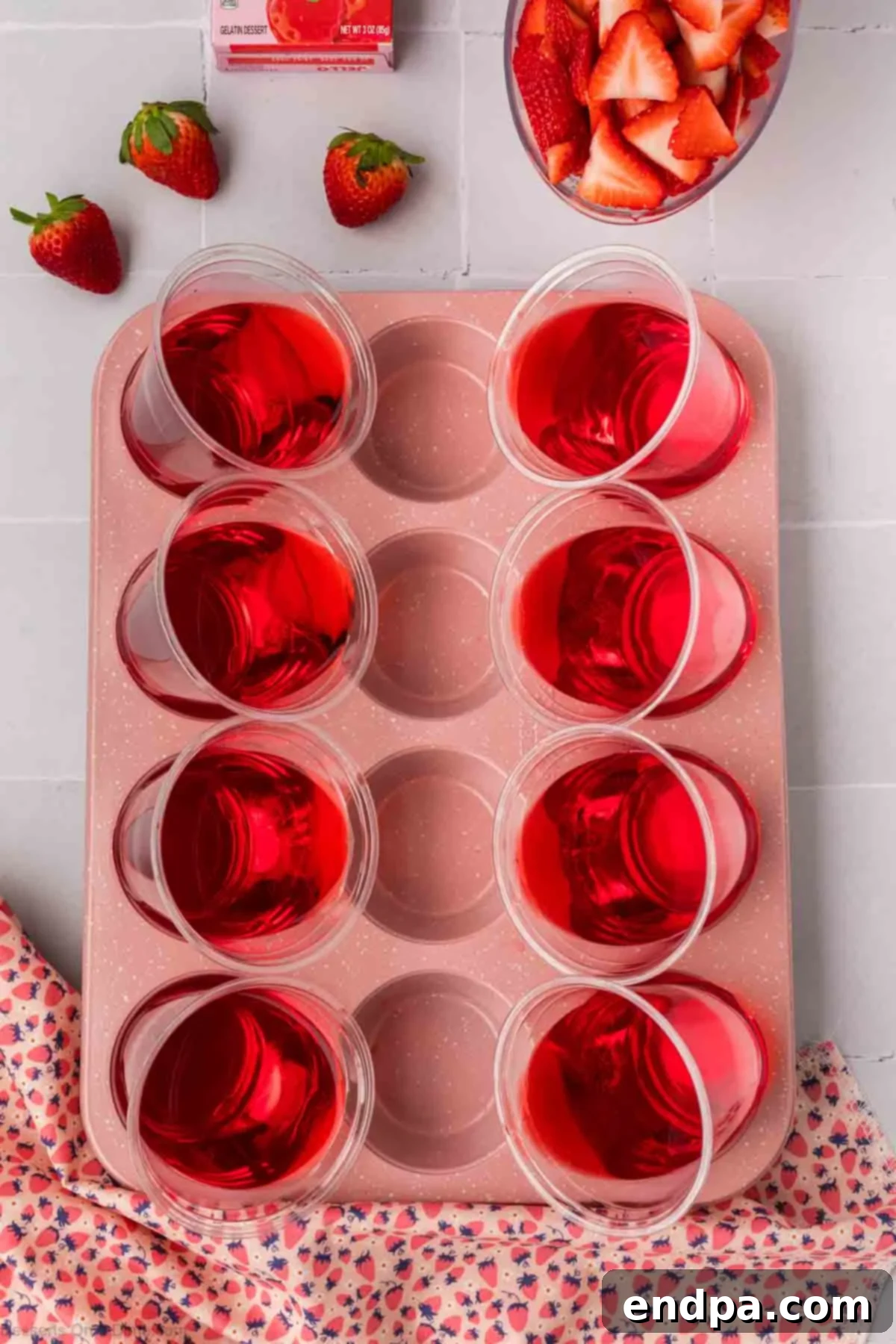 Strawberry Jello being poured into slanted cups in a muffin tin.