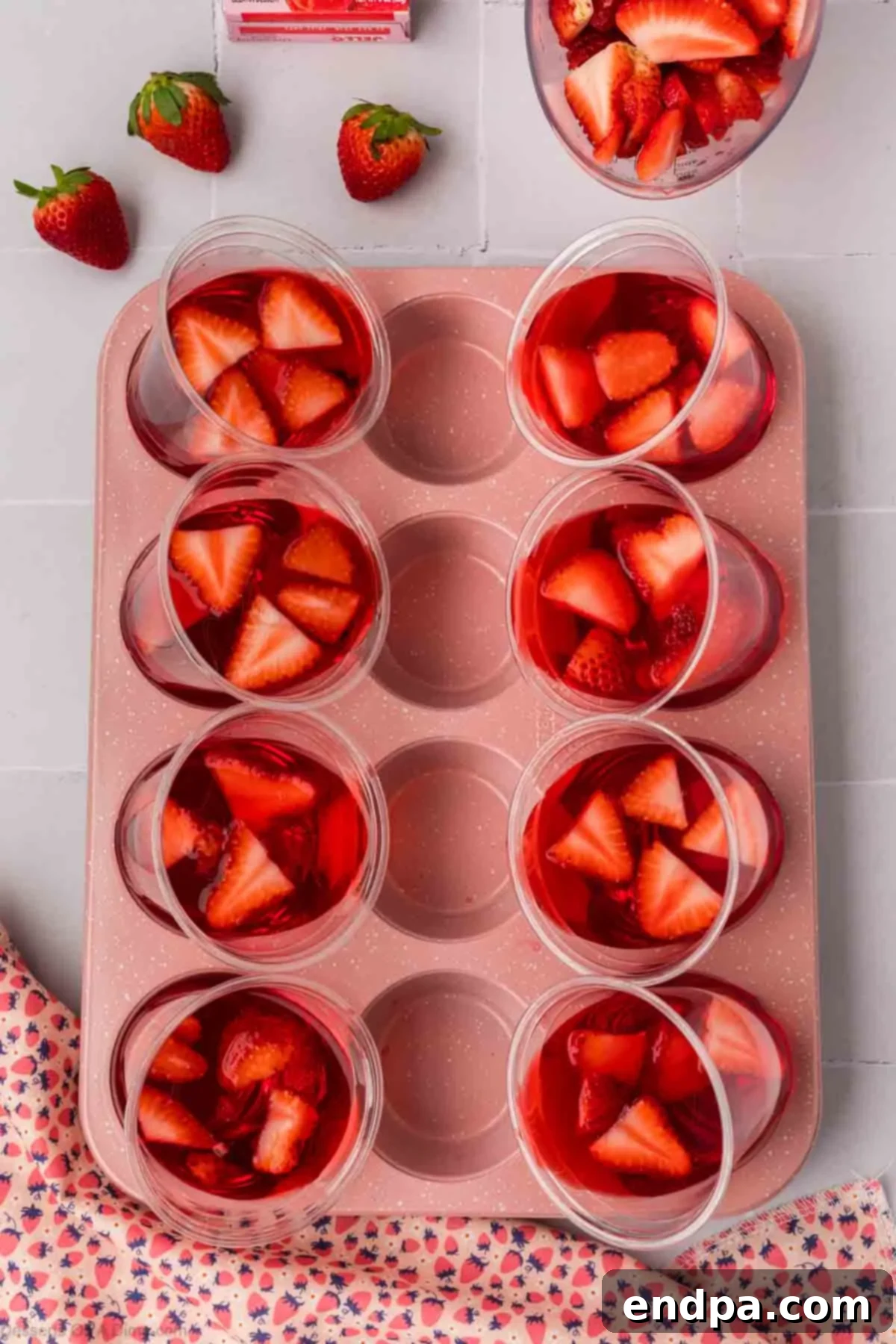 Strawberry slices floating in partially set Jello within a slanted cup.