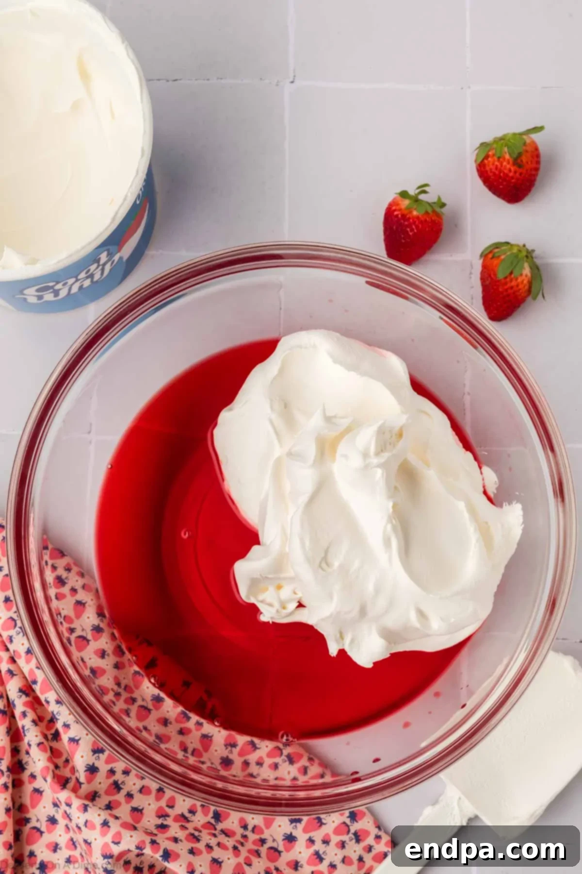 Cool Whip being folded into the cooled Jello mixture in a bowl.