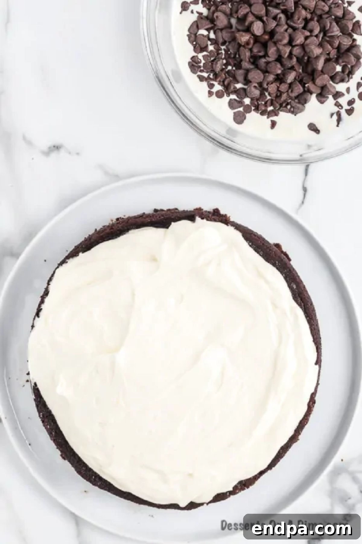The fluffy cream filling generously spread over the first layer of chocolate cake on a platter.