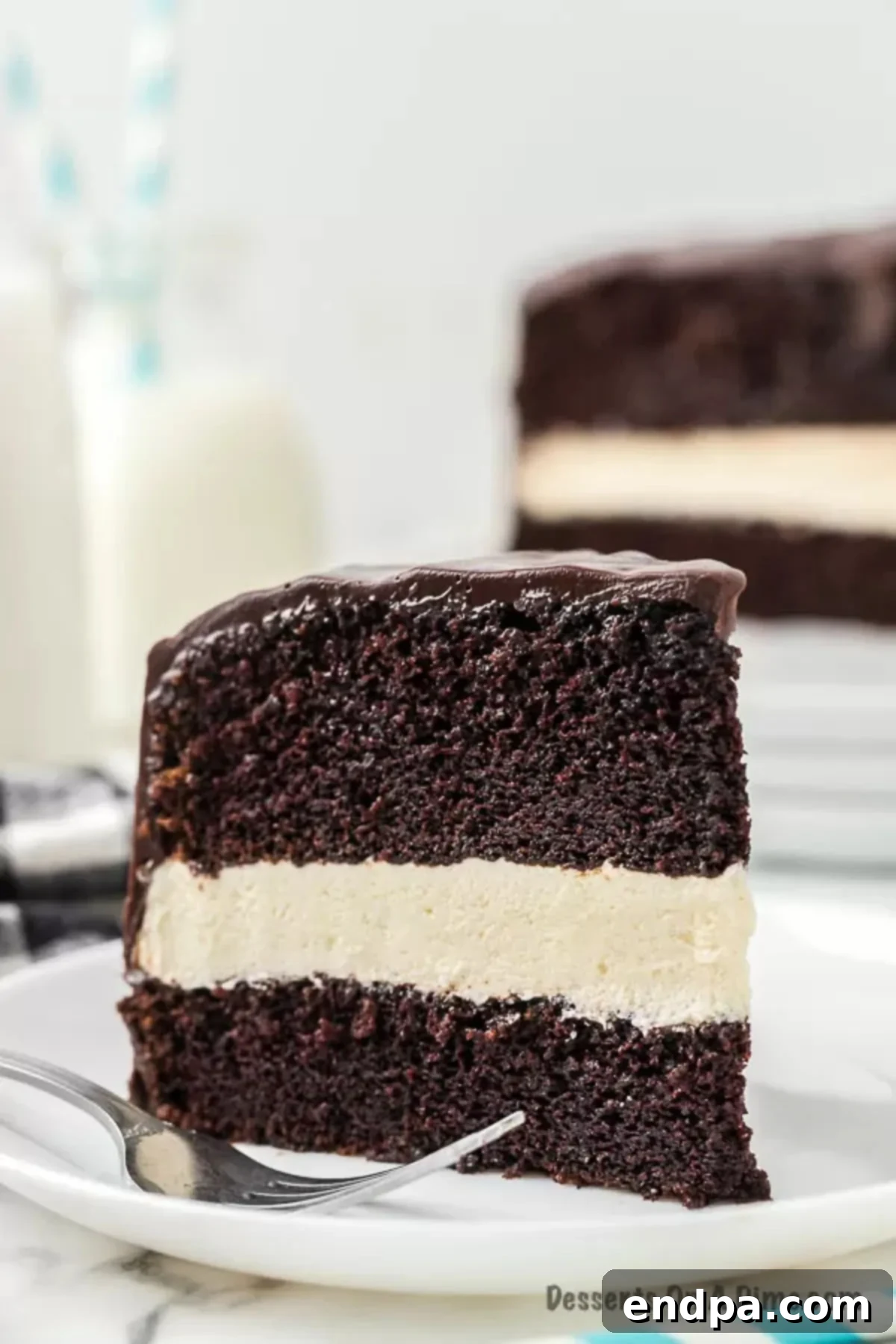 A perfectly sliced piece of Ding Dong Cake, showcasing the distinct layers of chocolate cake, white cream filling, and chocolate ganache, ready to be enjoyed.