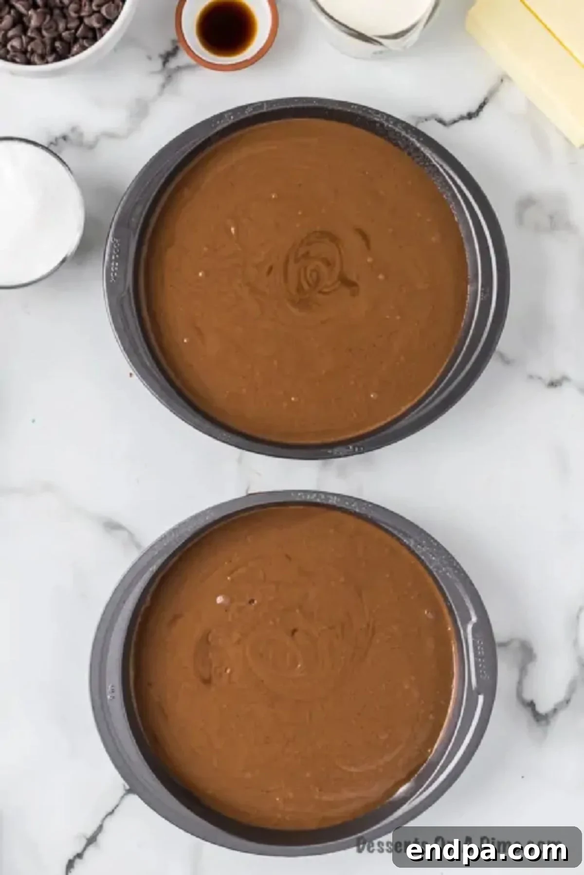 Chocolate cake batter being evenly poured into two round cake pans, ready for baking.