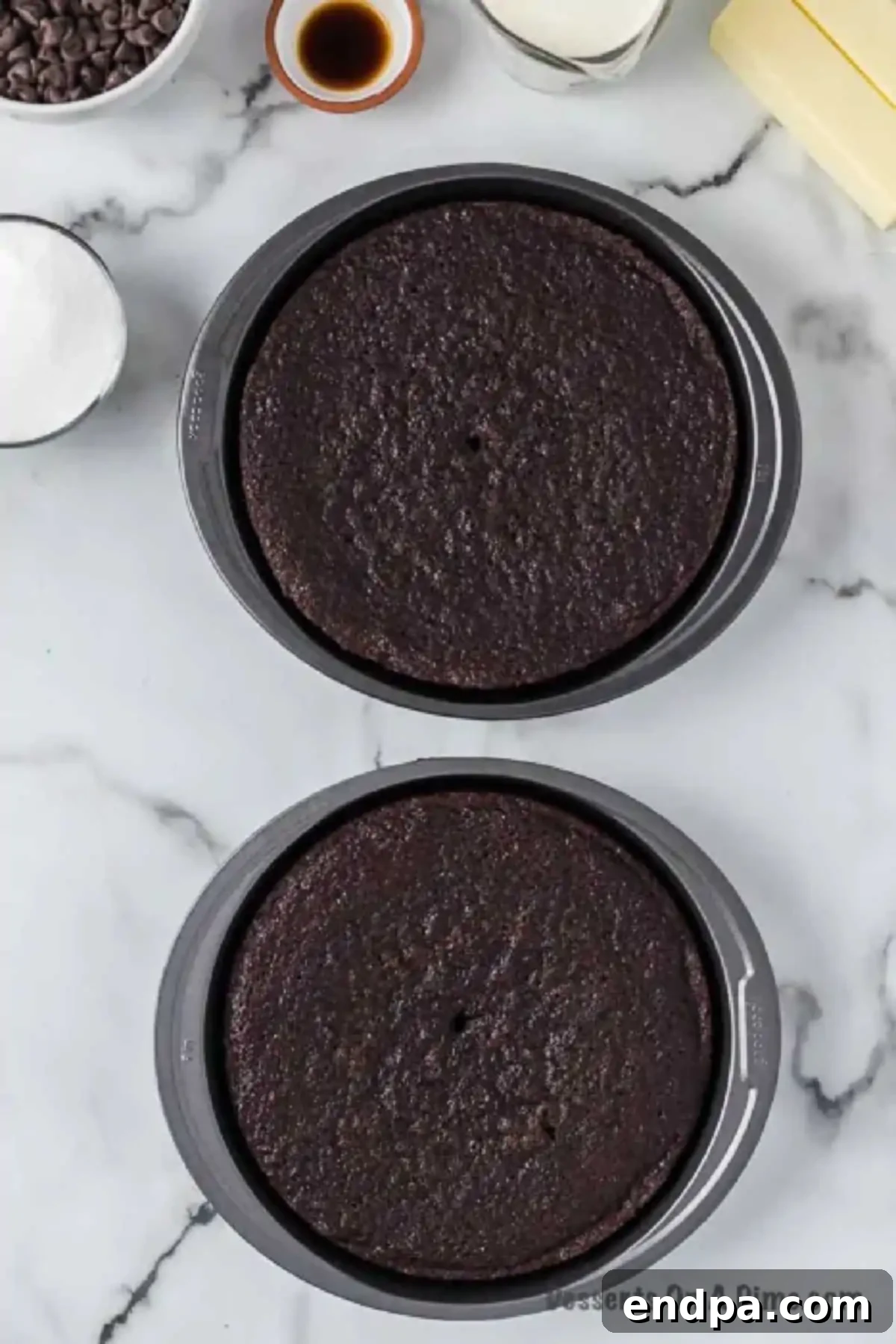 Two freshly baked chocolate cake layers cooling on a wire rack after being removed from the pans.