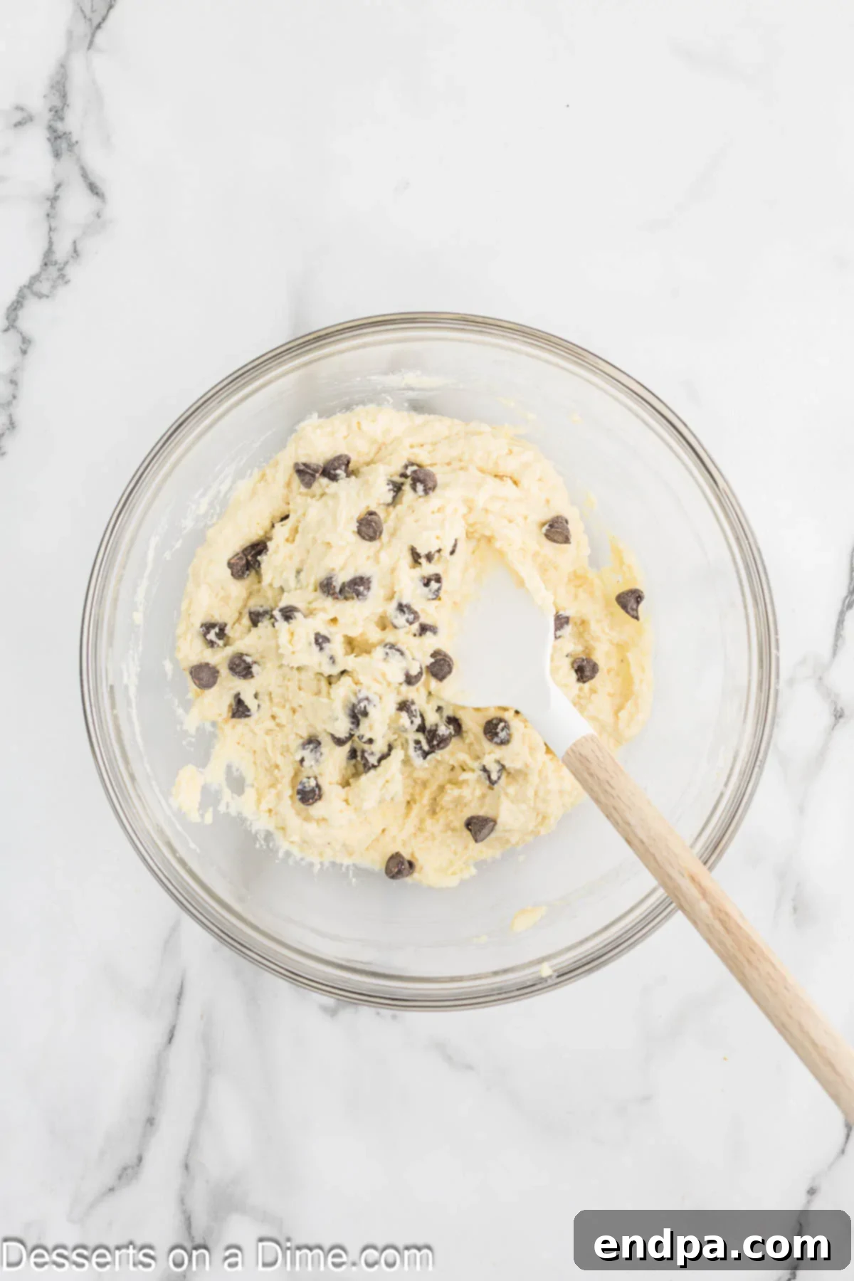 Sugar-free chocolate chips being gently folded into the cookie dough by hand.