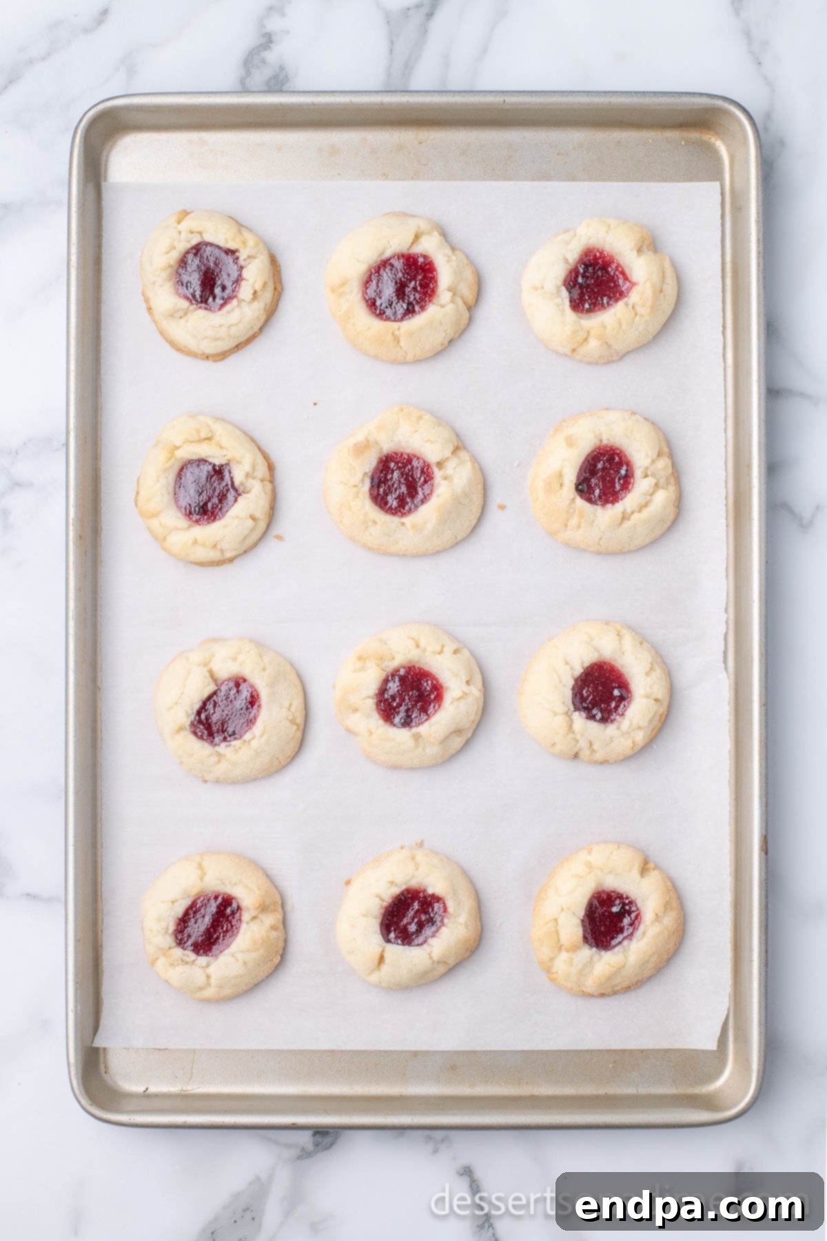 THUMBPRINT JAM COOKIES 11 Freshly baked Jam Thumbprint Cookies cooling on a wire rack after being removed from the oven.