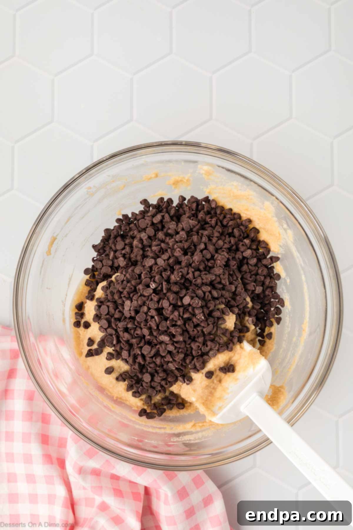 Mini chocolate chips are being gently poured into the prepared cookie dough mixture in the bowl, ready for the final step.