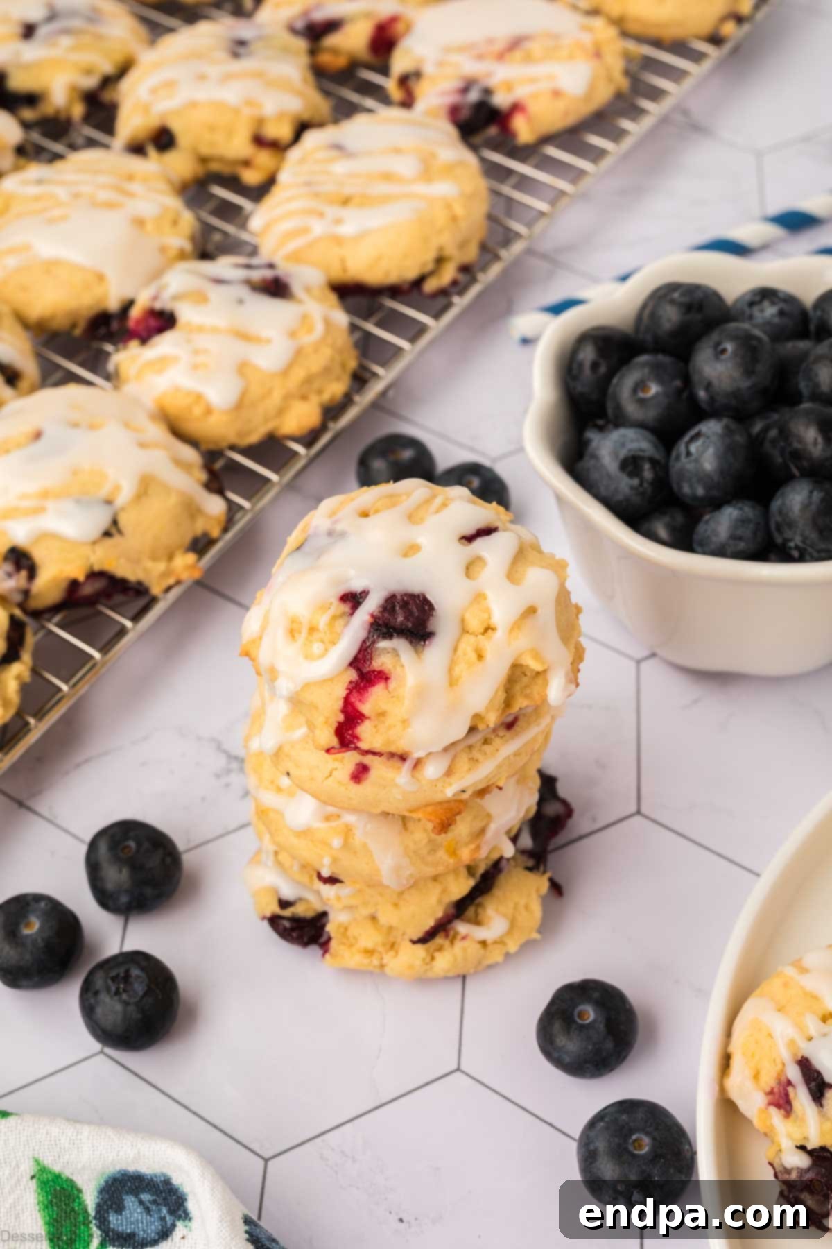 Stacked lemon blueberry cookies with a generous lemon glaze, highlighting their soft texture and juicy blueberry bursts.