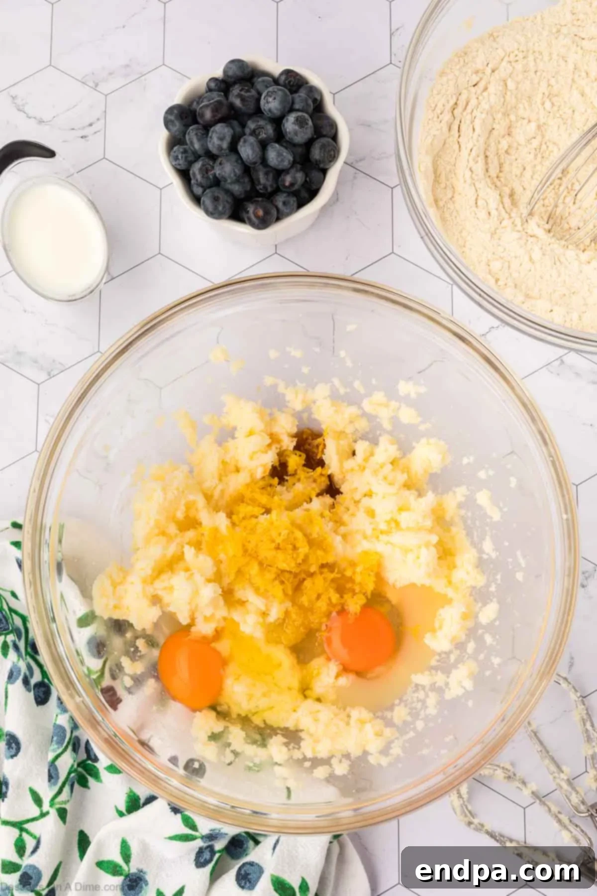 Wet ingredients, including eggs, vanilla extract, lemon zest, and lemon juice, being mixed into the creamed butter and sugar mixture.