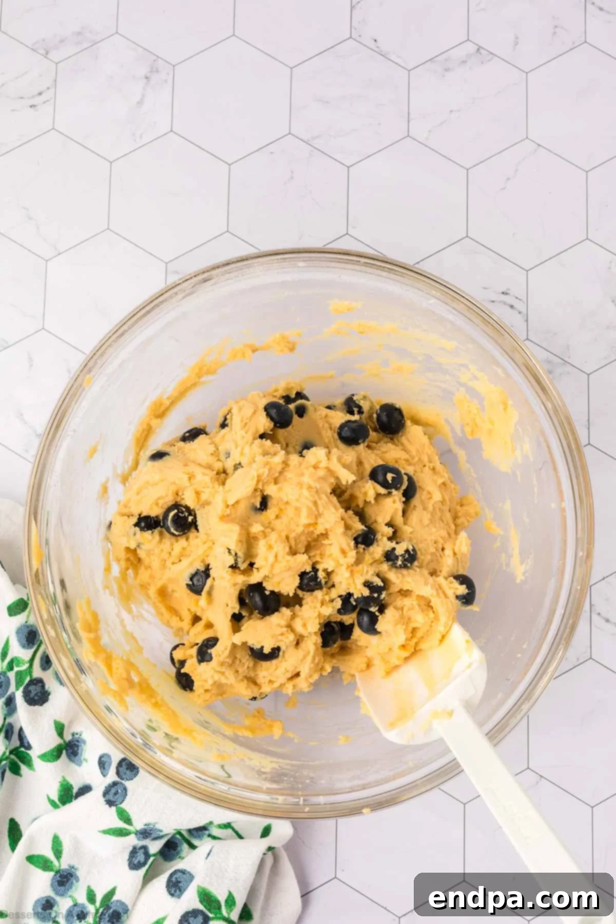 Fresh blueberries being gently folded into the prepared cookie dough using a rubber spatula.